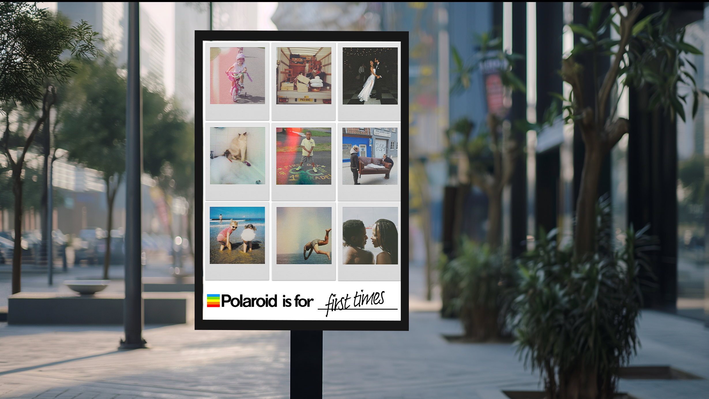 A large vertical photo display on an outdoor sidewalk, featuring a grid of nine different photographs. The photos include a girl riding a bicycle, a truck loaded with boxes, a woman in a white dress dancing, a cat, a child playing hopscotch, a sofa with a person, two children at the beach, a person doing a gymnastics flip, and a close-up of two people facing each other. The bottom of the display reads, "Polaroid is for first times" with the Polaroid logo.