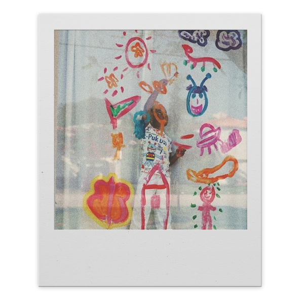 Child drawing colorful doodles and characters on a transparent surface, including a smiling face, a sun, clouds, and various abstract shapes.