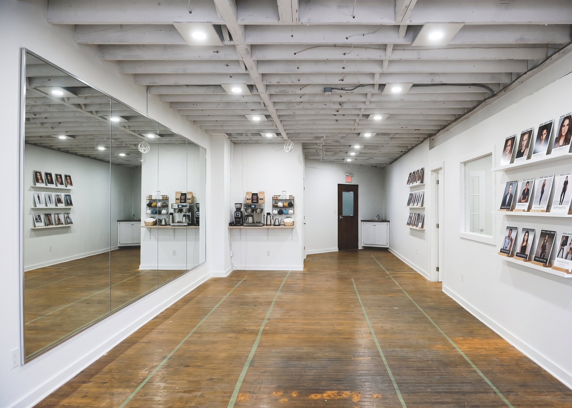 Empty retail space with white walls, wooden floors, large mirror, framed photos of models, coffee stations, and ceiling with exposed beams and recessed lighting.