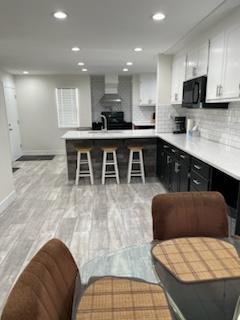Modern kitchen with white cabinets, black lower cabinets, white countertops, a breakfast bar with three stools, and a brown dining chair in the foreground.