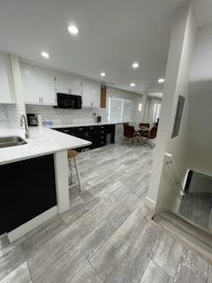 Modern open-concept kitchen with white cabinets, black appliances, and gray tiled flooring, adjacent to a dining area with chairs.