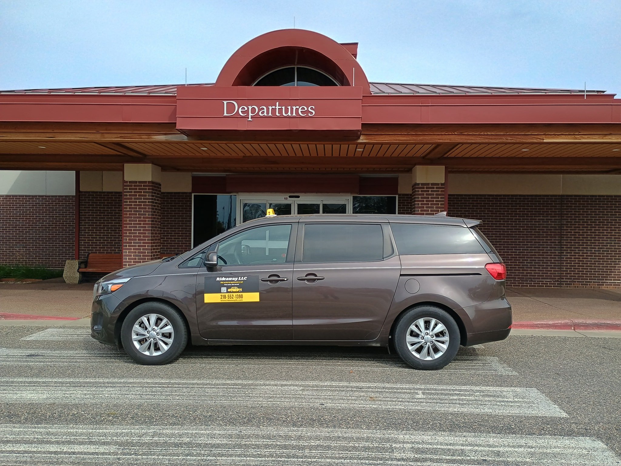 Grey minivan parked in front of an airport terminal with a sign that says 'Departures'