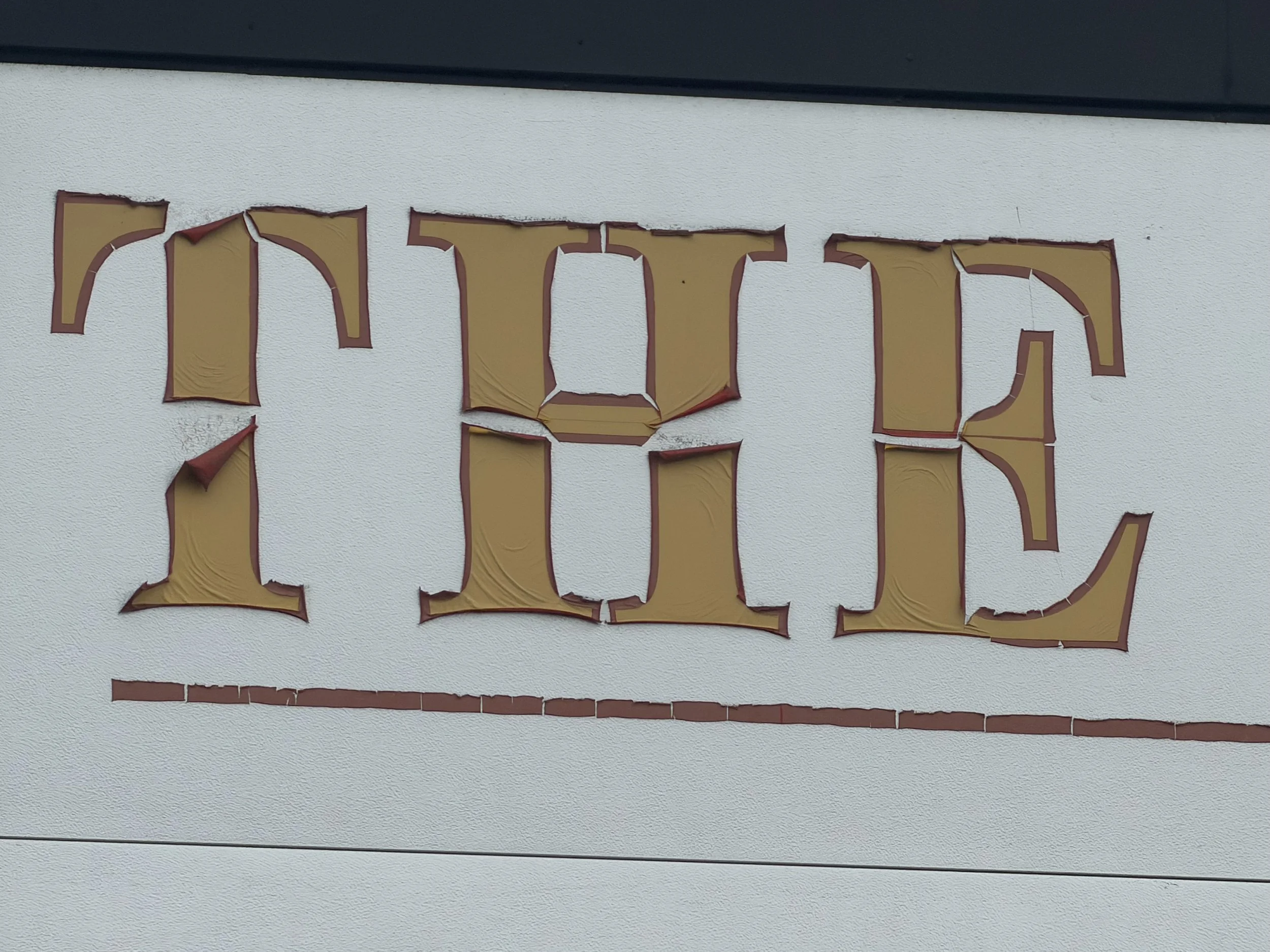 Part of a weathered, yellow sign with red edges mounted on a white textured wall.
