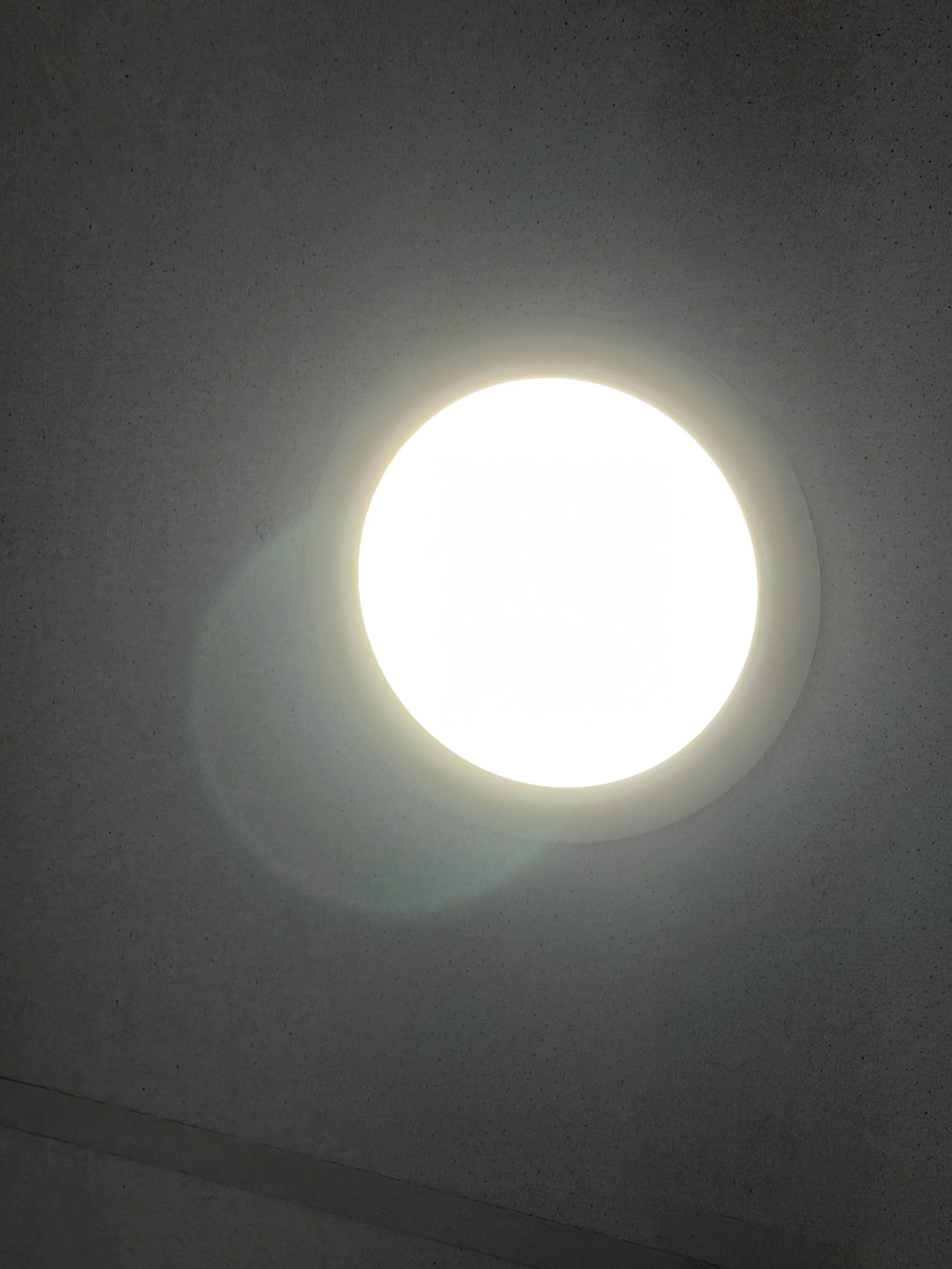 Close-up of a round, white ceiling light fixture on a textured ceiling, illuminated