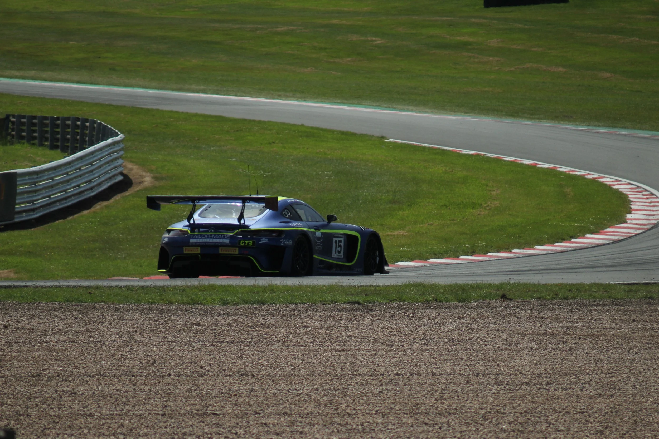 A racing car on a race track with green grass on either side and safety barriers, in a racing environment.
