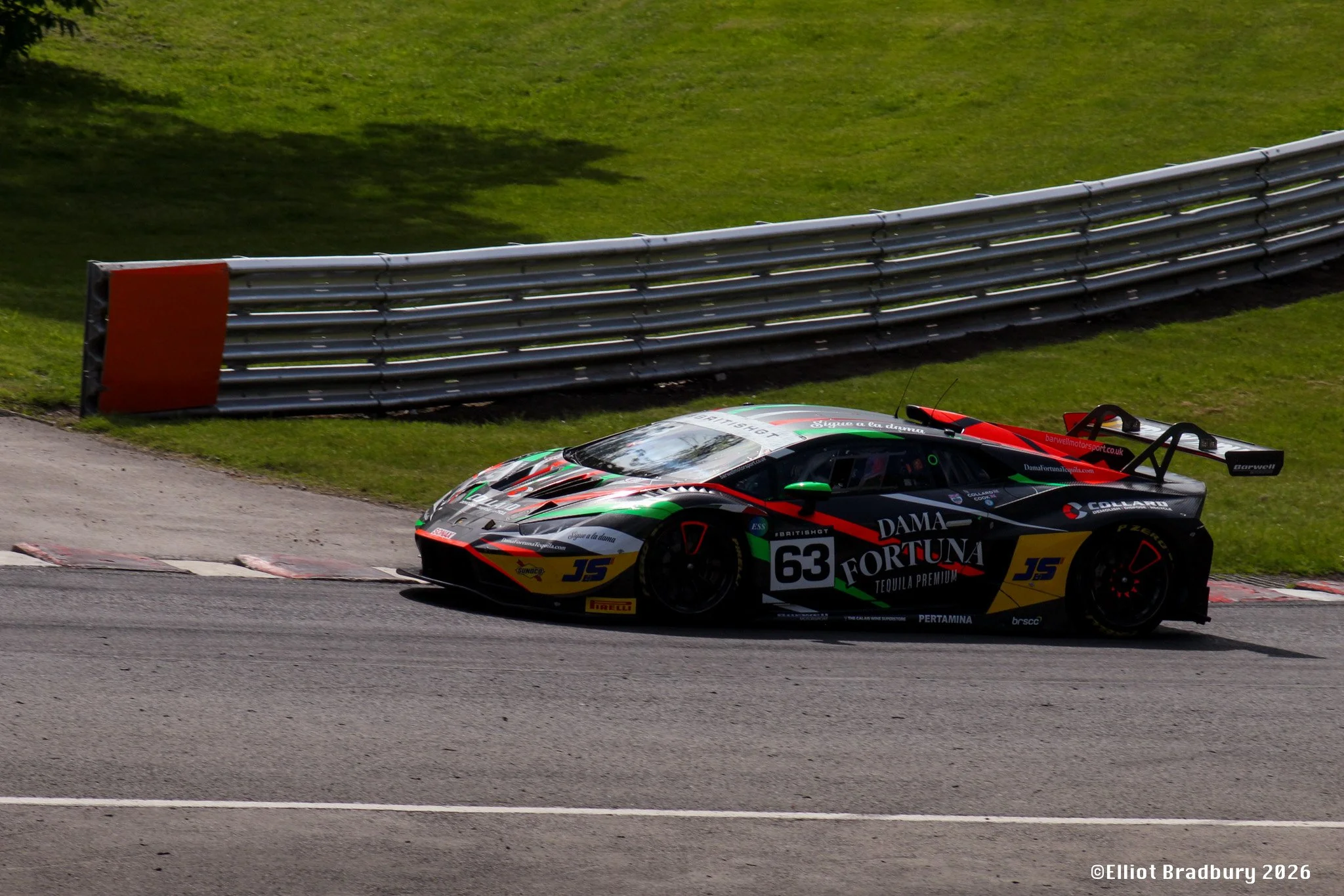 A race car on a track, with a barrier and grass in the background.