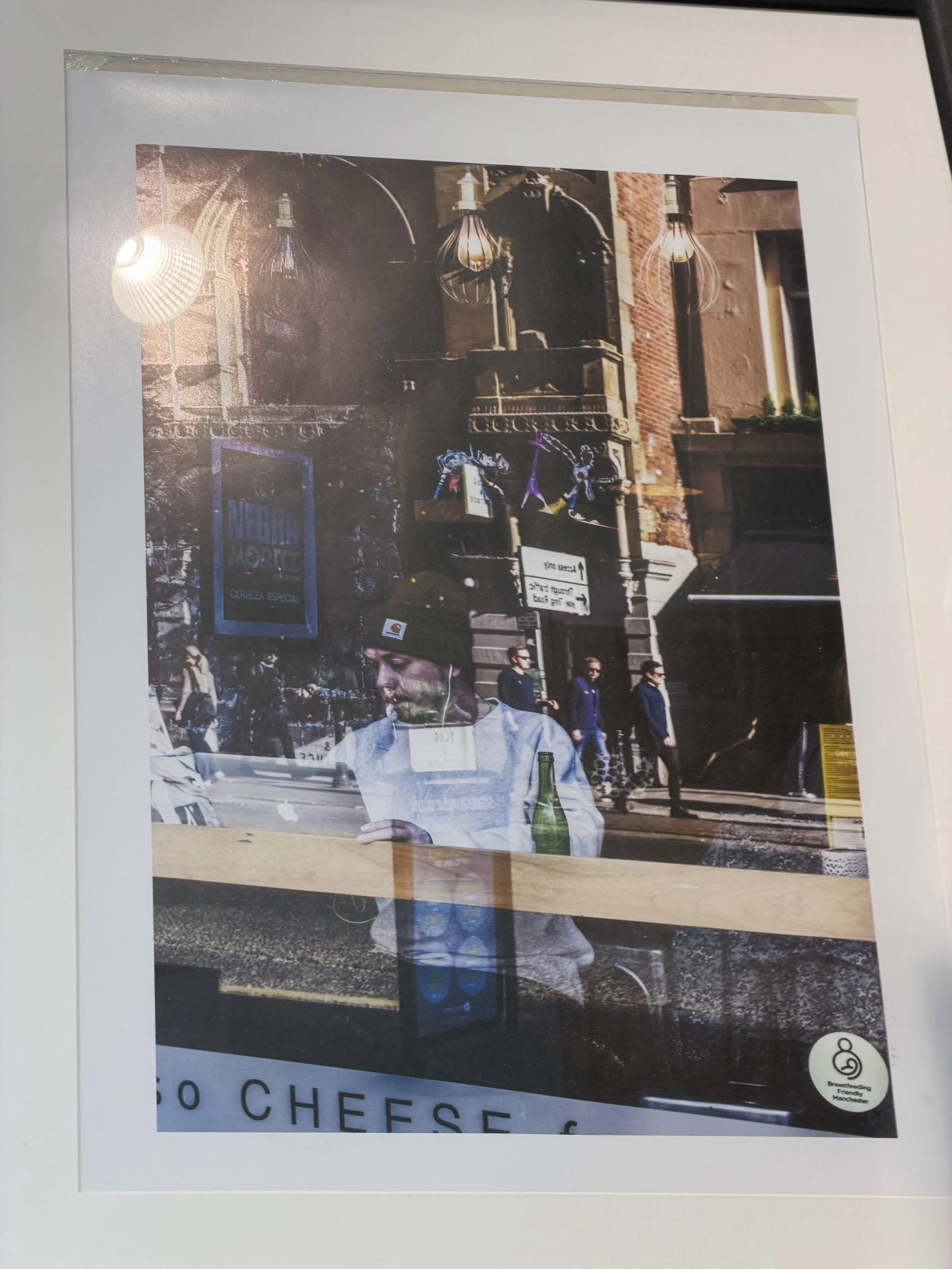 A poster showing a person with a beard and long hair looking at a paper or menu. Behind the person, there is a city street scene with pedestrians walking by, architectural brick buildings, and various street signs. The poster has text that reads 'SO 