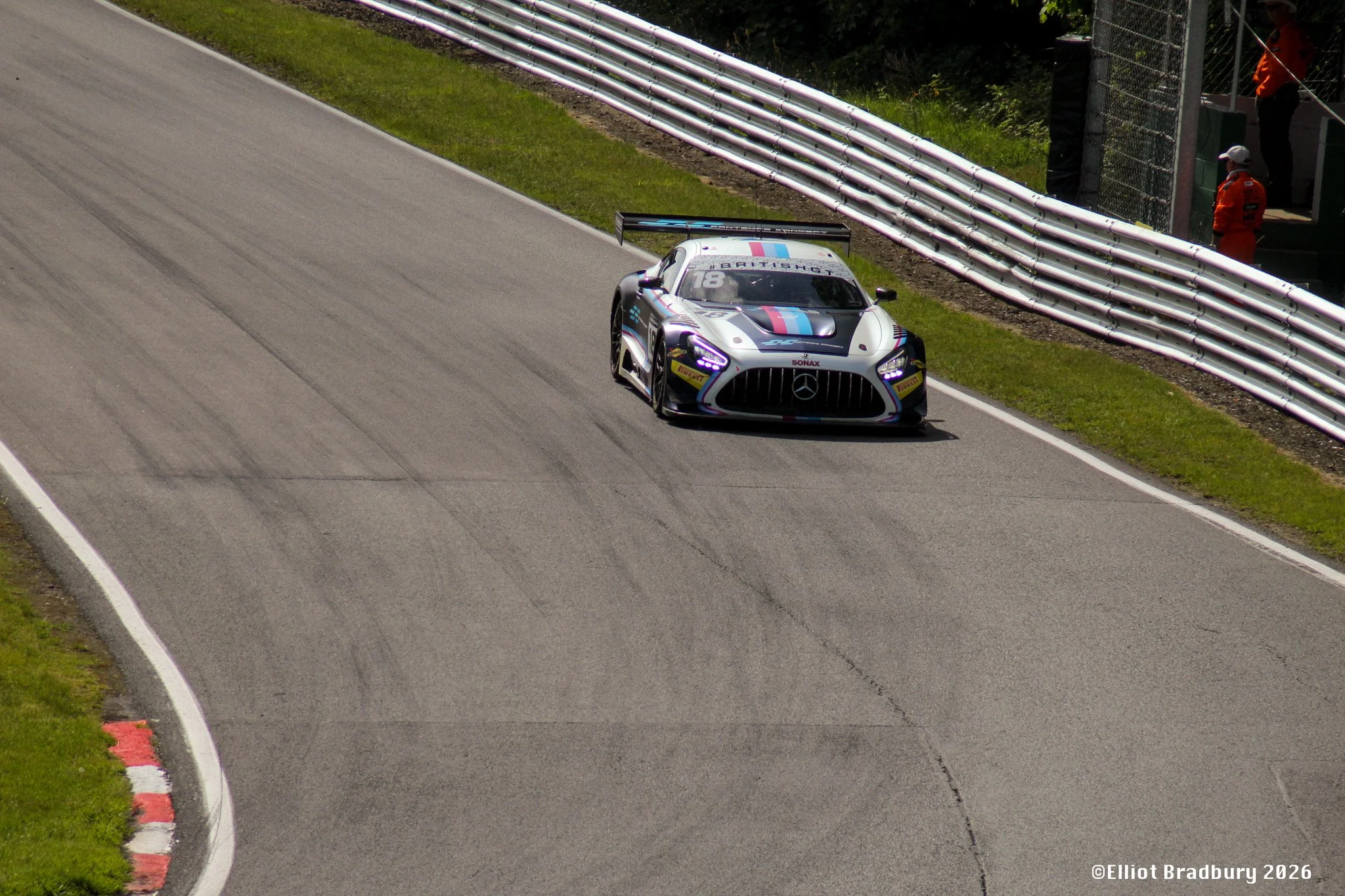 A race car on a race track near a barrier with race officials watching from the side.