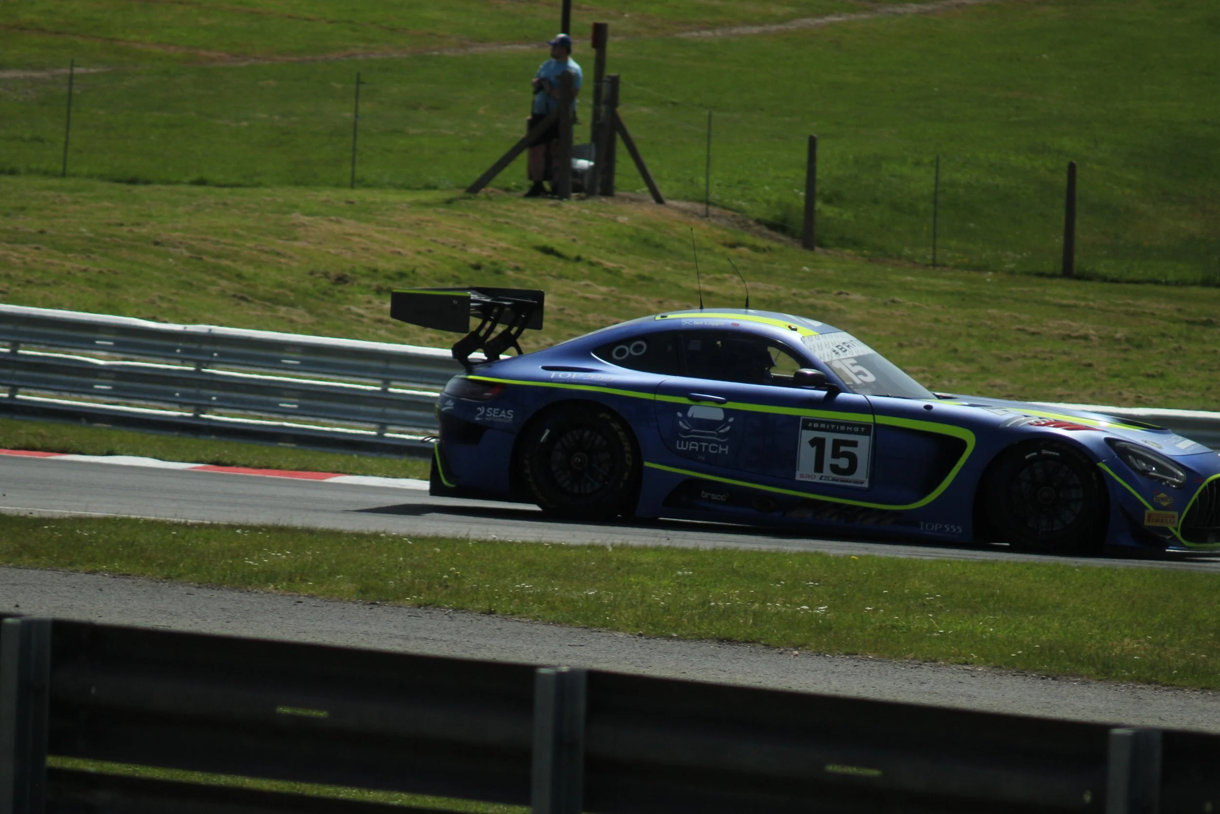 A race car on a racetrack with a person standing on a hill in the background, watching the event.