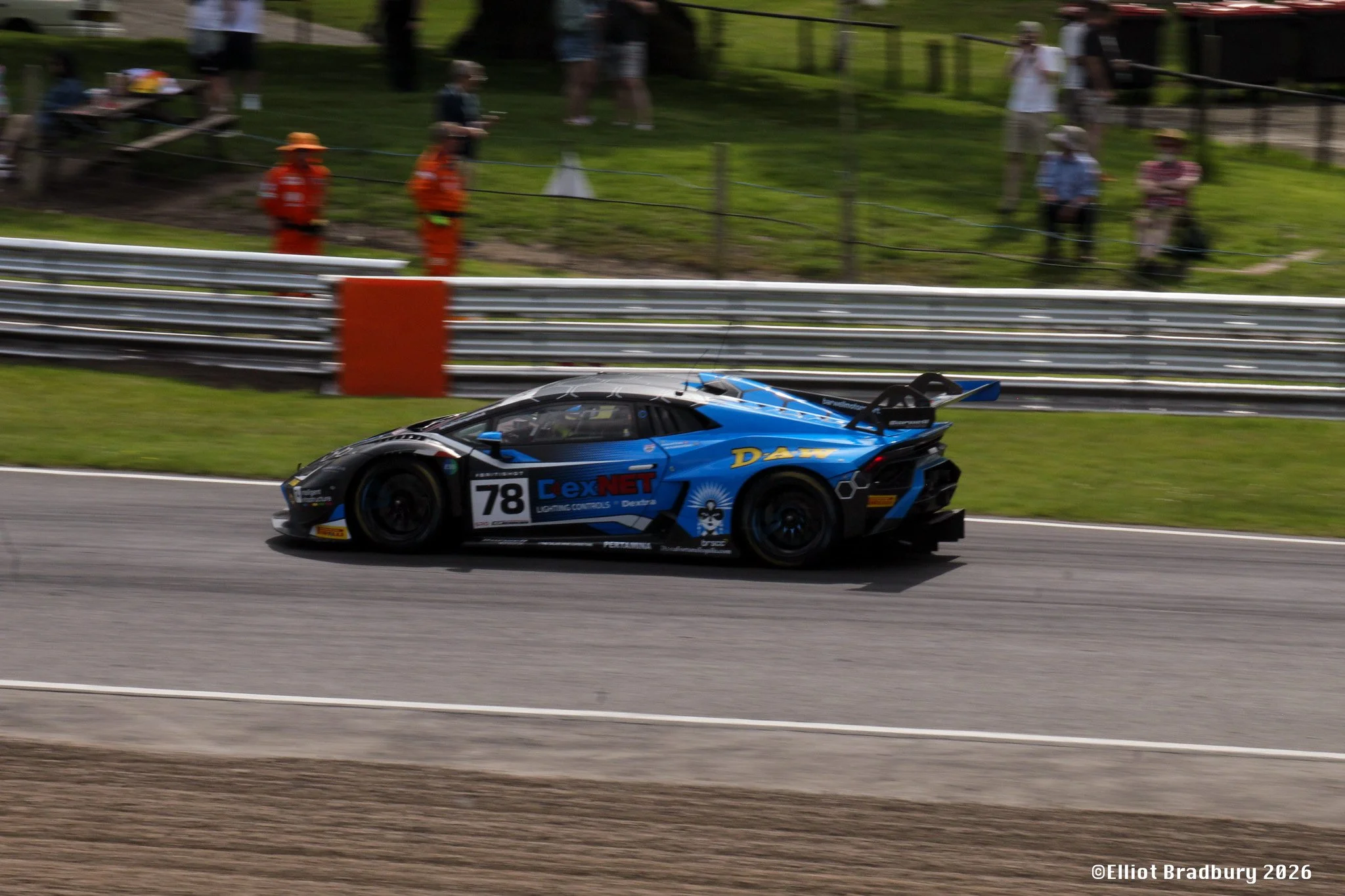 A blue race car with the number 78 on the side driving on a race track, with a chain-link fence and spectators in the background.