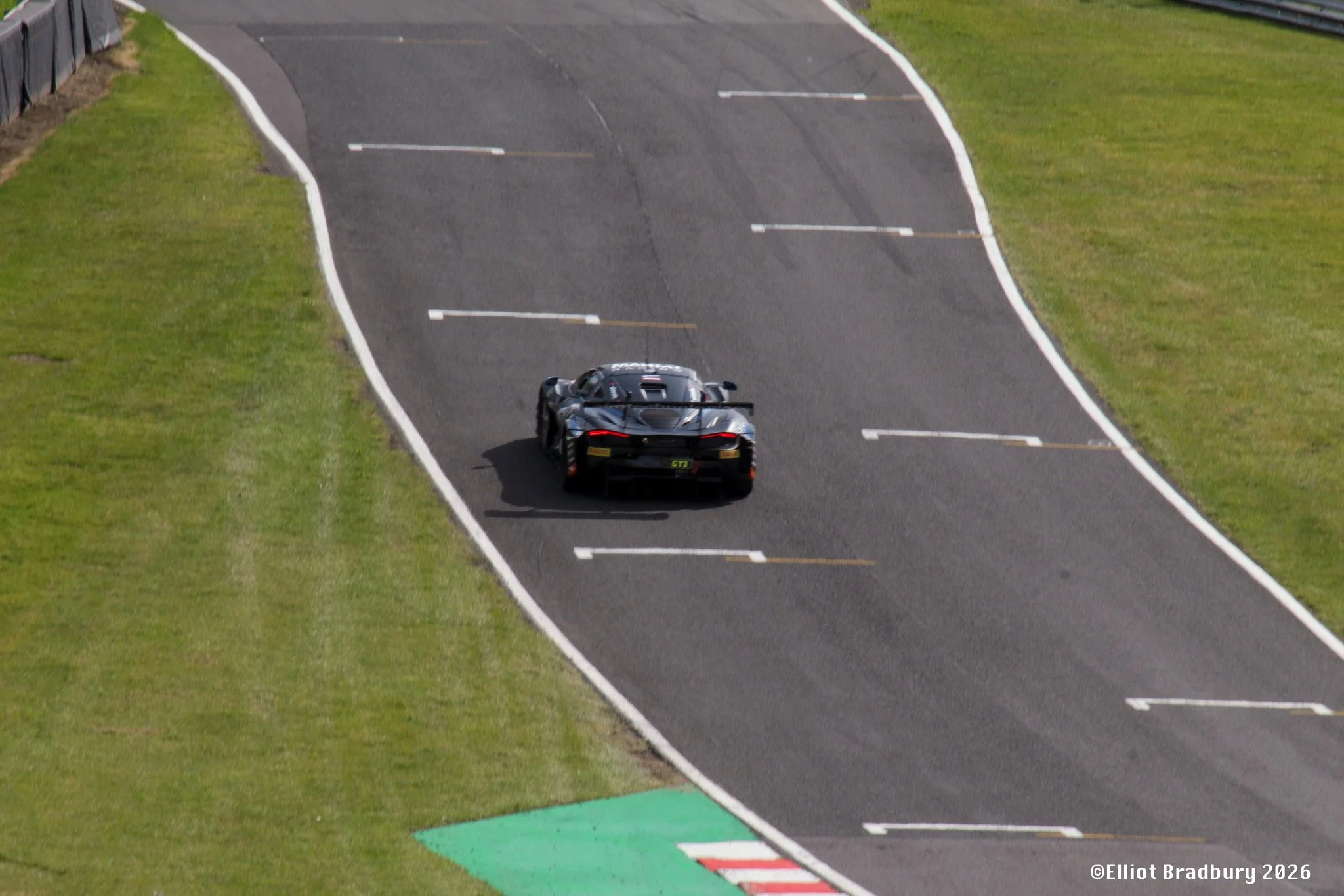 A black racing car on a race track with yellow and white markings, surrounded by green grass on both sides.