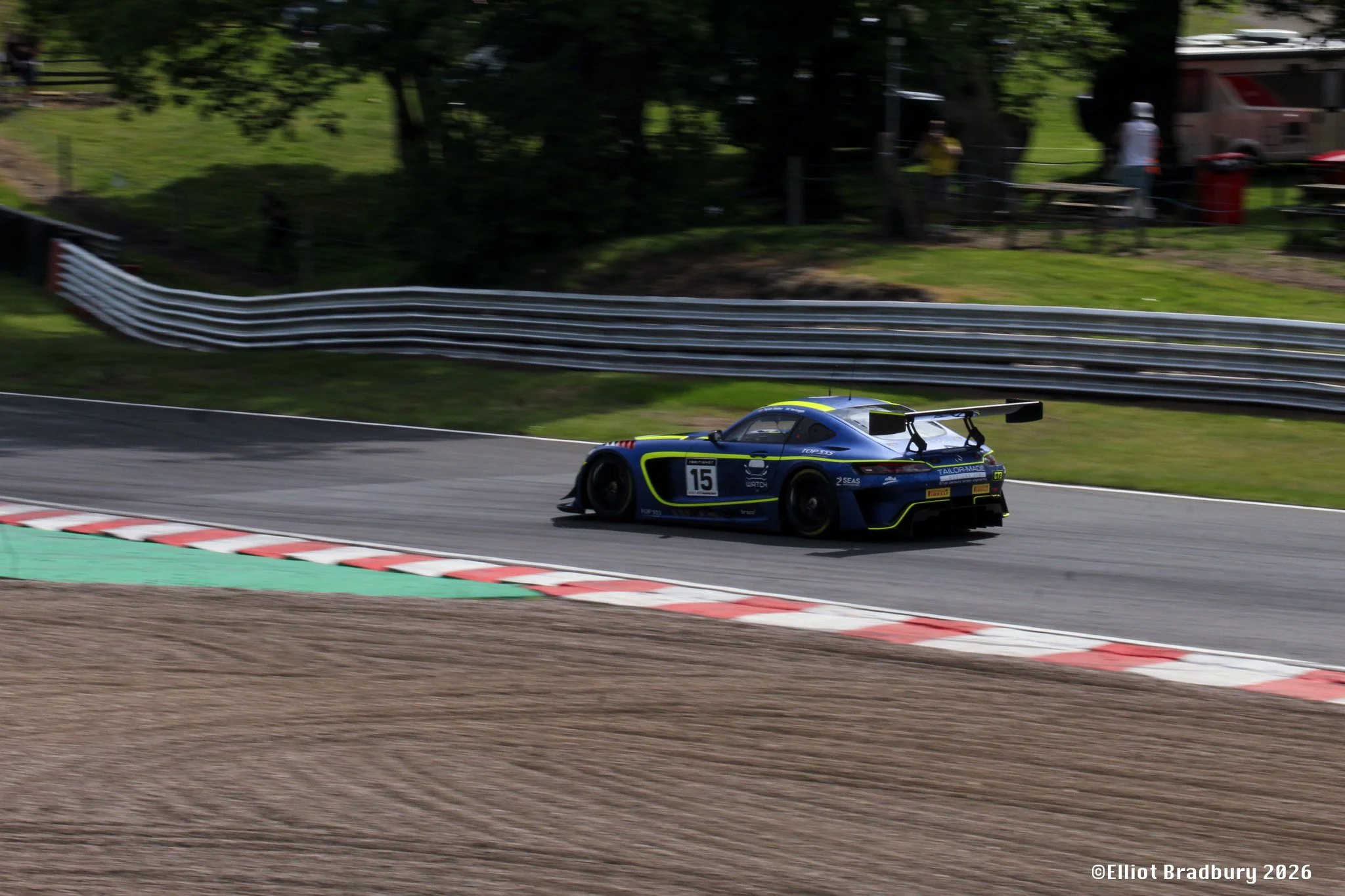 Race car on a race track during a race, with spectators and trees in the background.