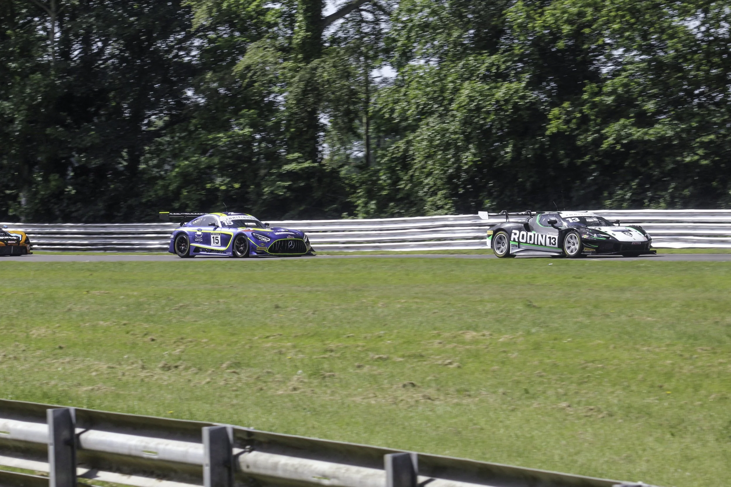 Race cars driving on a track surrounded by green trees in the background.