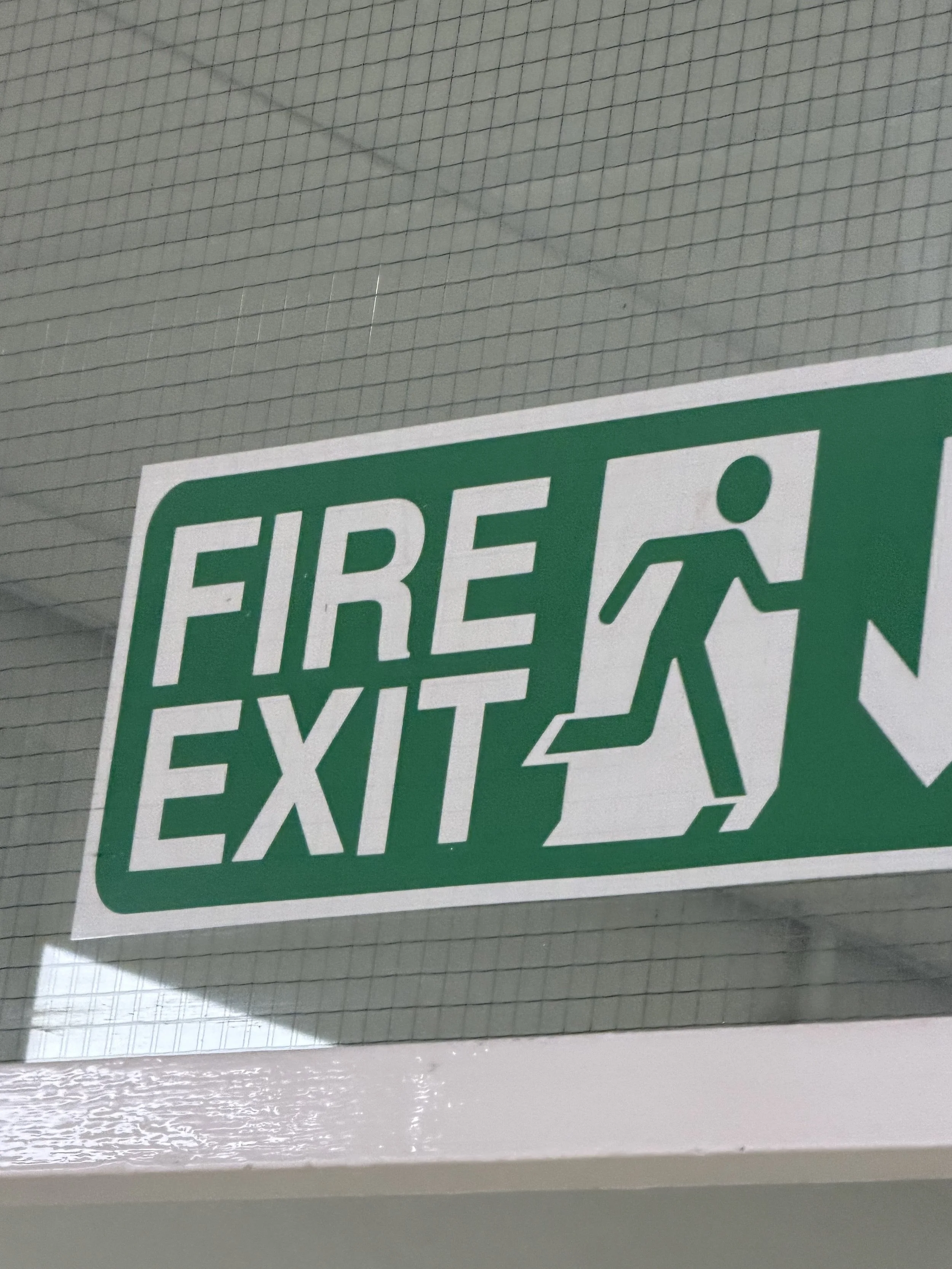Green emergency exit sign with a running person icon and the word 'FIRE' visible, mounted on a white tiled ceiling.