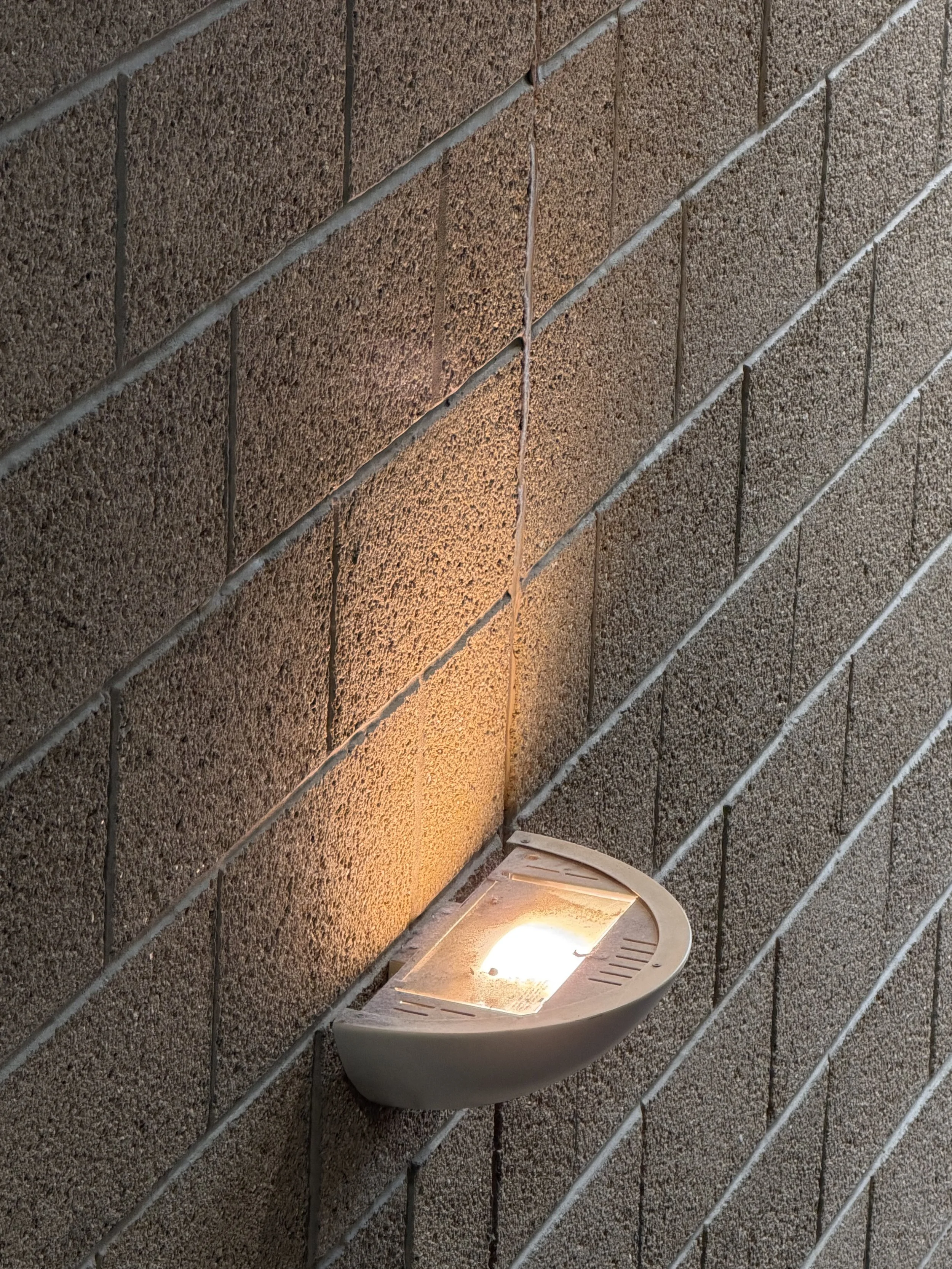 A wall-mounted outdoor light fixture with a glowing bulb, attached to a textured brick wall.