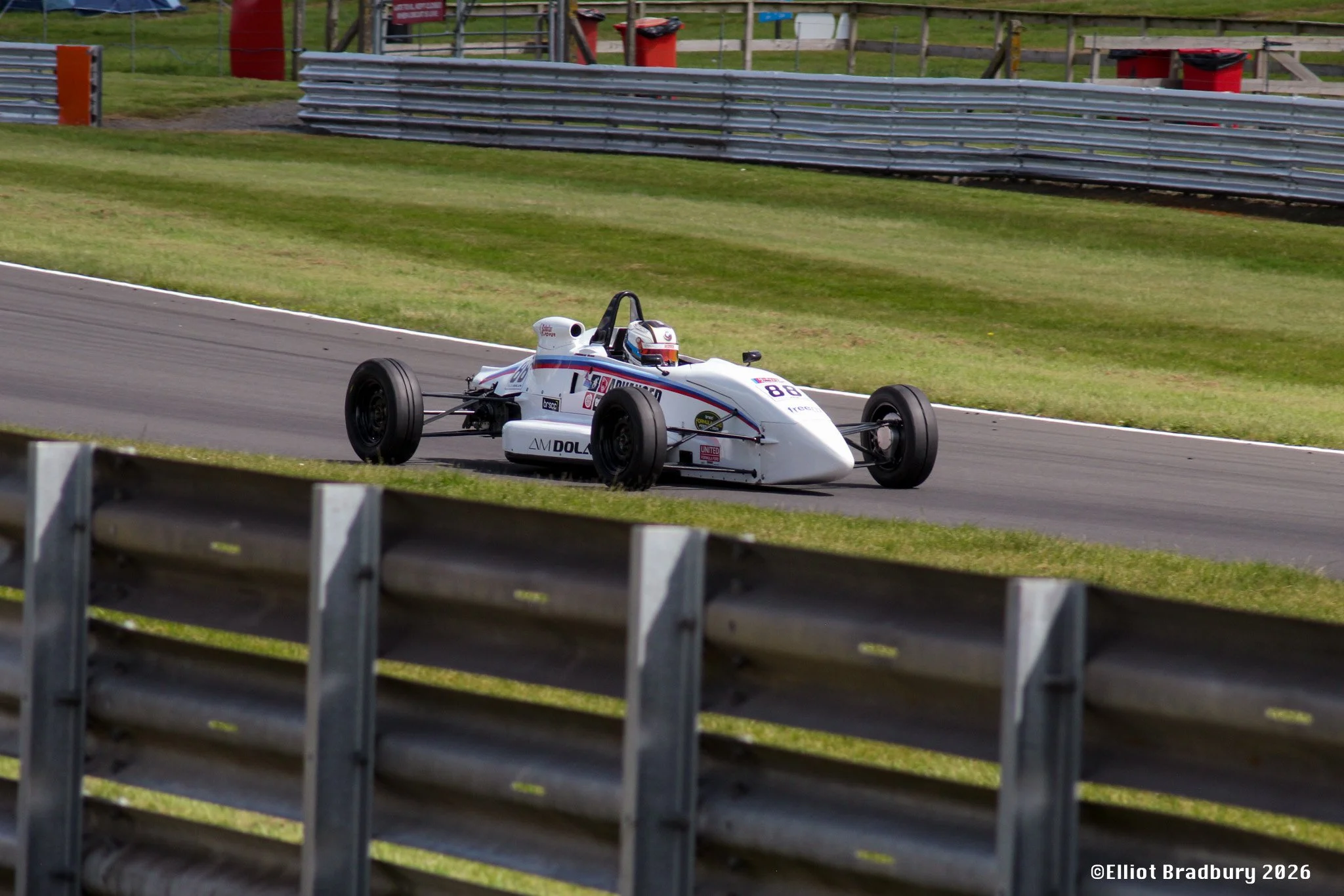A white racing car on a race track with multiple sponsor logos and the number 88, with a grassy area and safety barriers in the background.