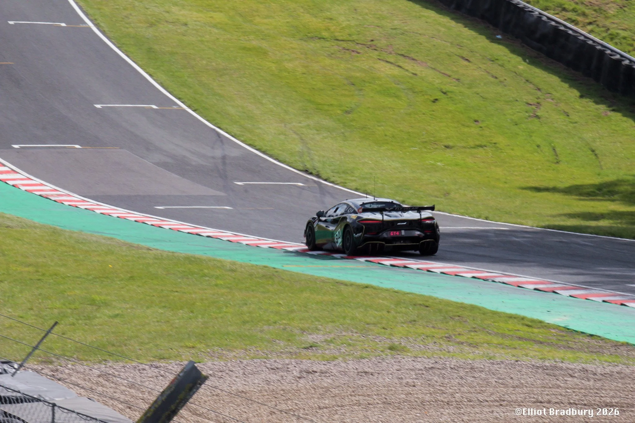 A sleek black race car is driving on a winding race track surrounded by green grass and barriers, with a section of marker paint at the curve's edge.