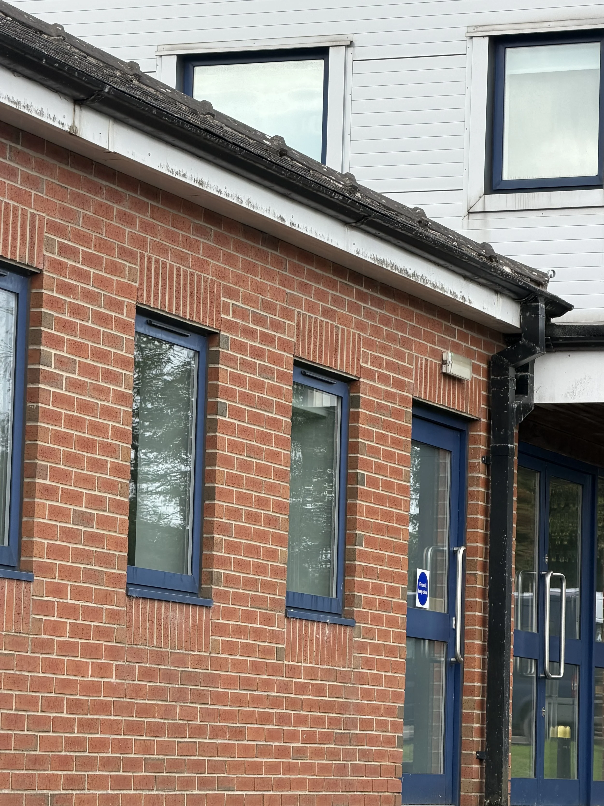 Close-up of a building's exterior showing red brick wall and blue-framed windows with black trim, along with a glass door with a metal handle and a sign indicating it is a fire escape.