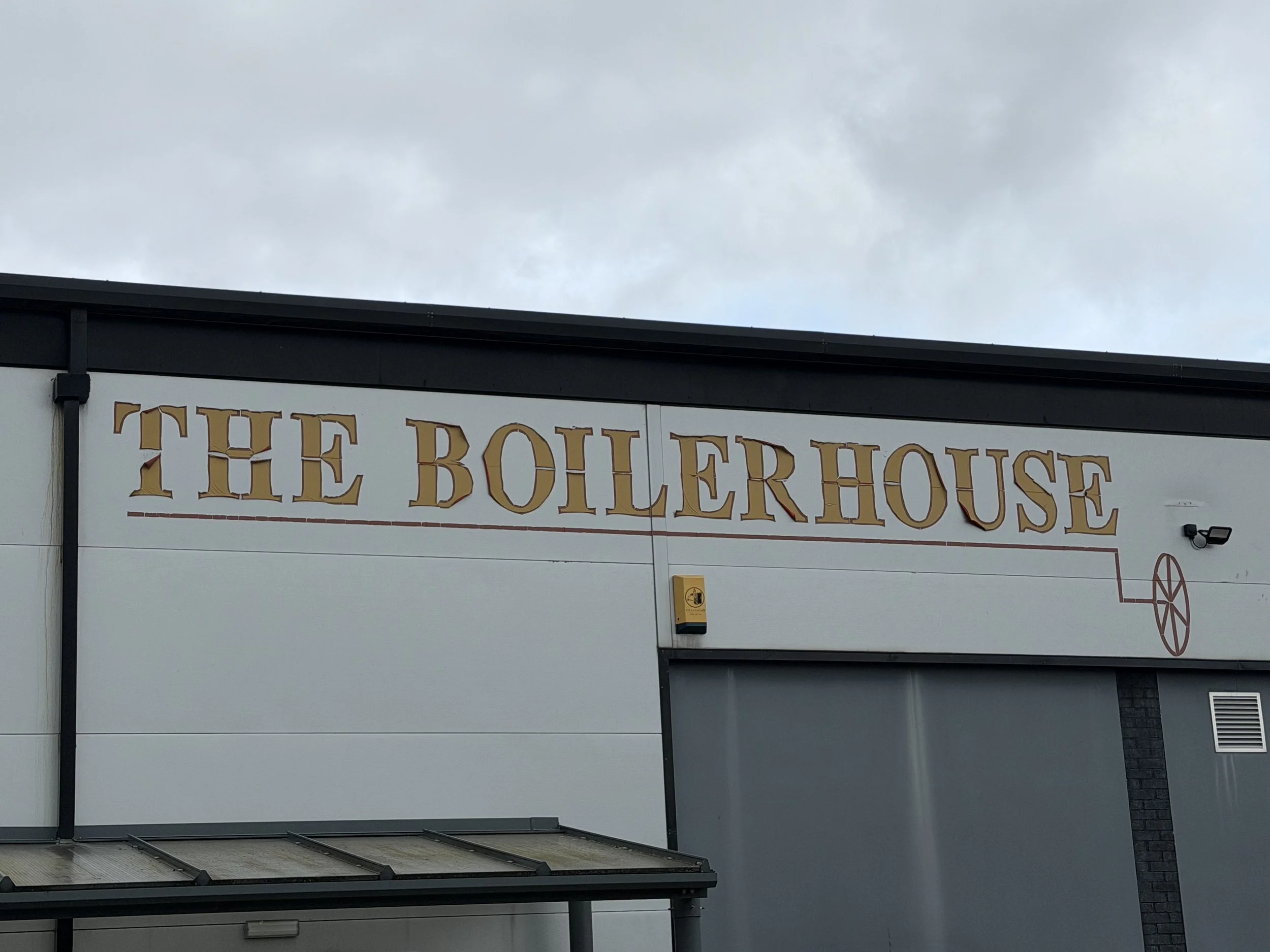The exterior of a building with a large sign reading 'The Butterhouse' in gold and brown letters, and a snow wheel symbol, beneath a cloudy sky.