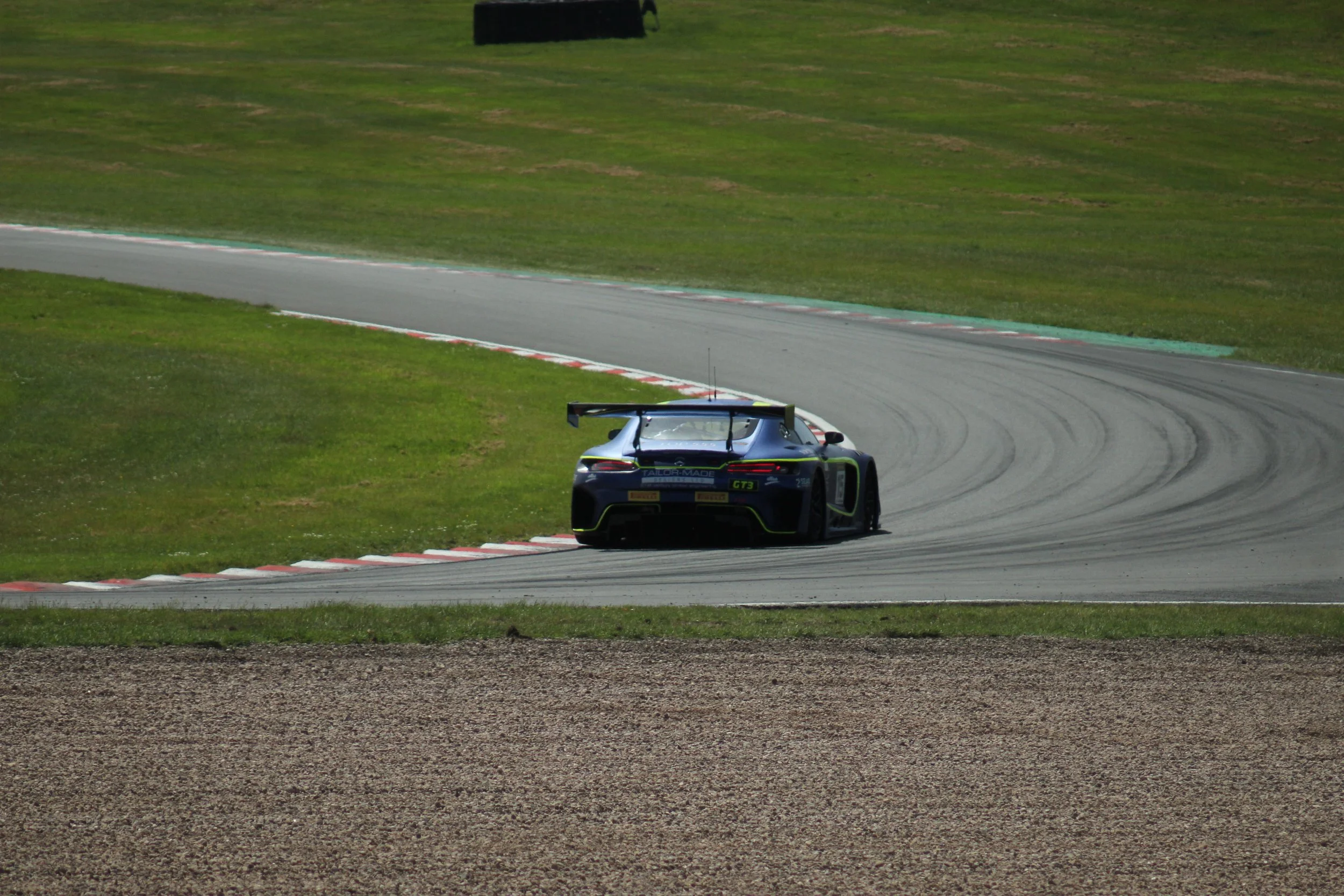 A race car driving on a curving race track surrounded by grass and gravel.