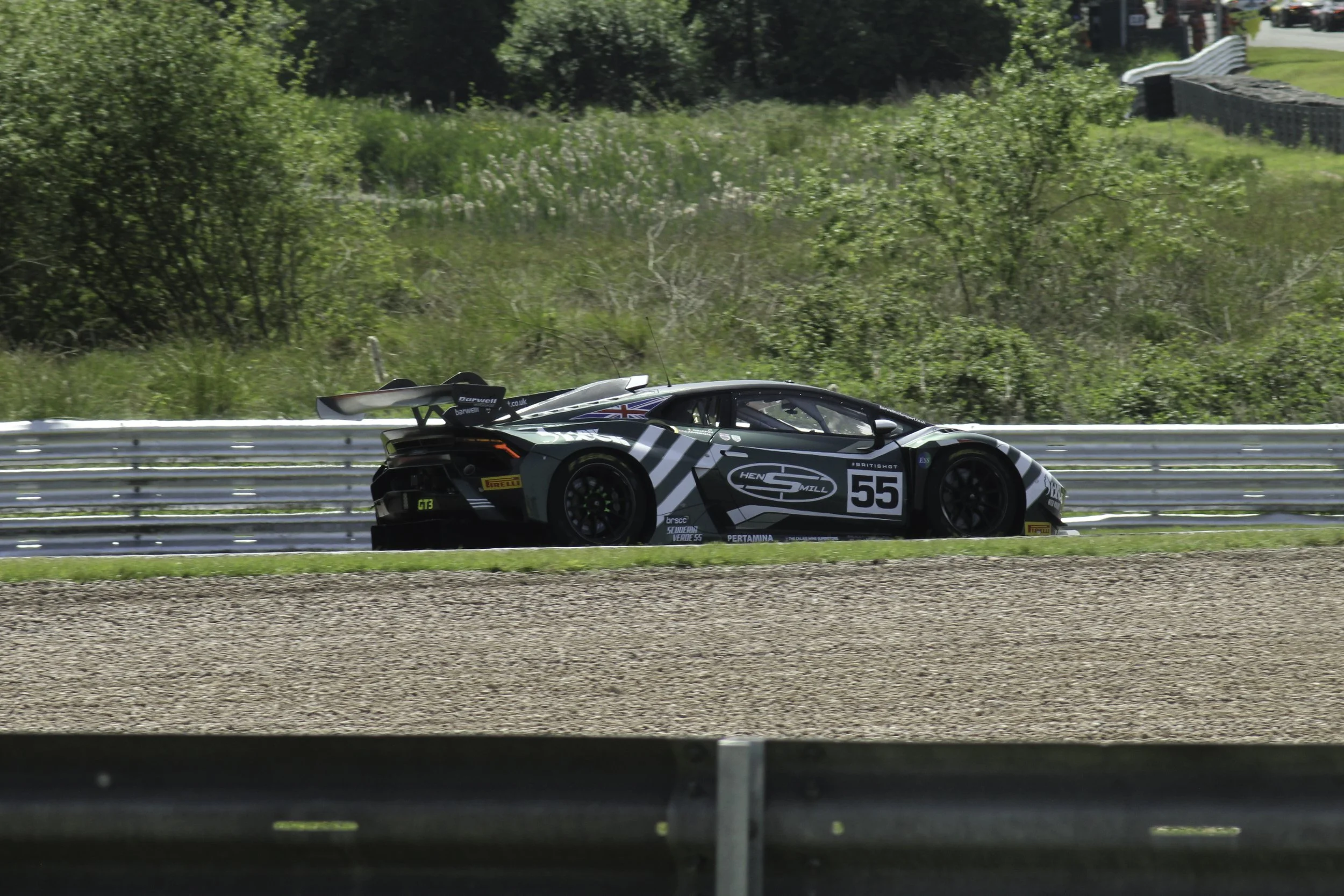 A racing sports car on a race track with green trees and a grassy hillside in the background.