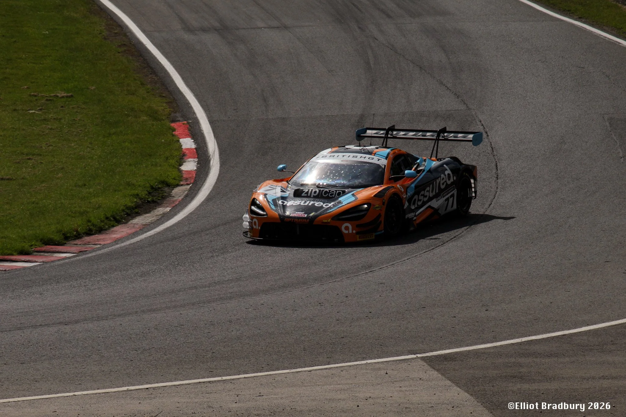 A racing car on a track navigating a sharp turn, with grass on the side, during daytime.