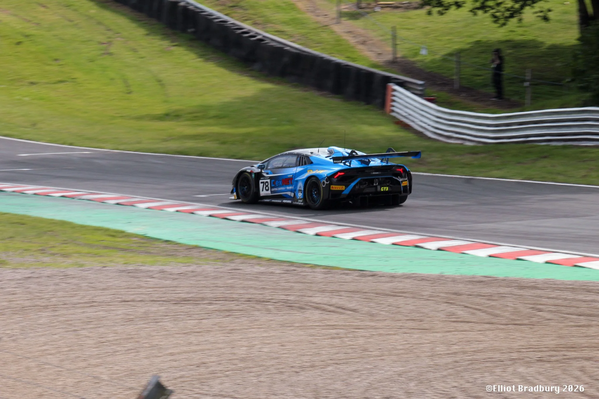 A blue race car with the number 78 on it speeds around a race track, with a black and white barrier on the side and green grass beyond.