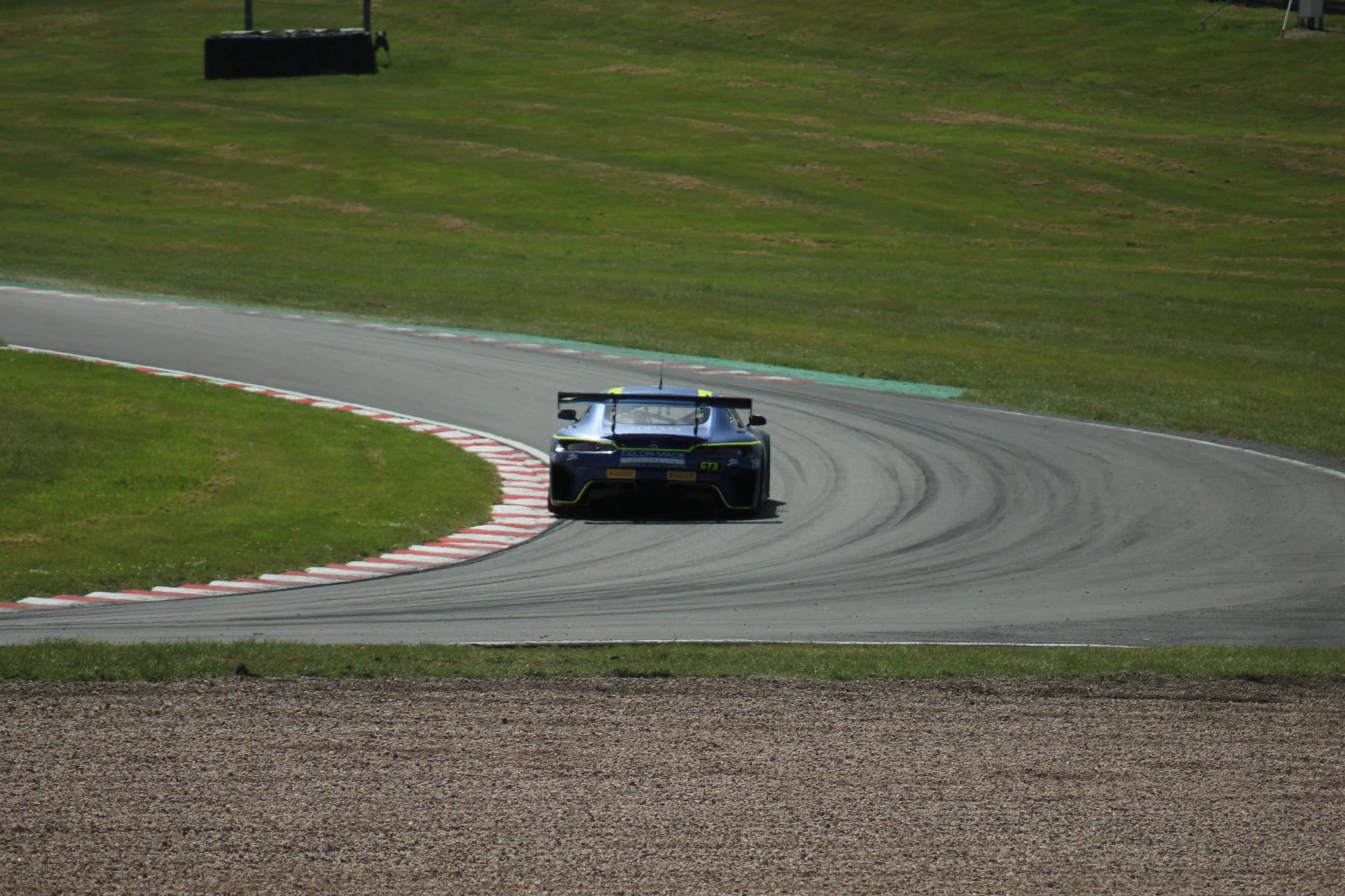 An electric race car driving on a curving race track surrounded by grass and minimal infrastructure.