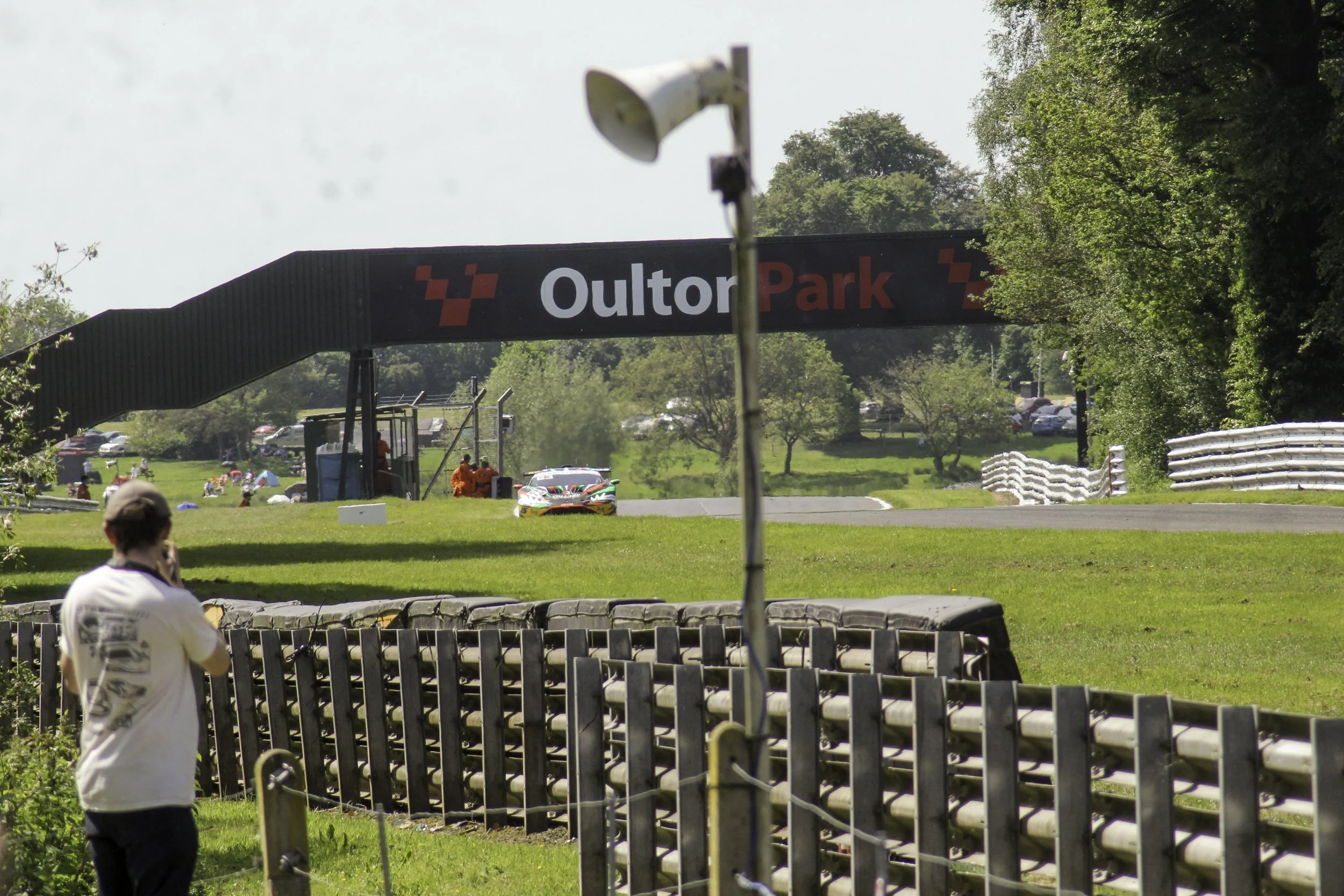 Race car on track at Outor Park with spectators and greenery in the background.
