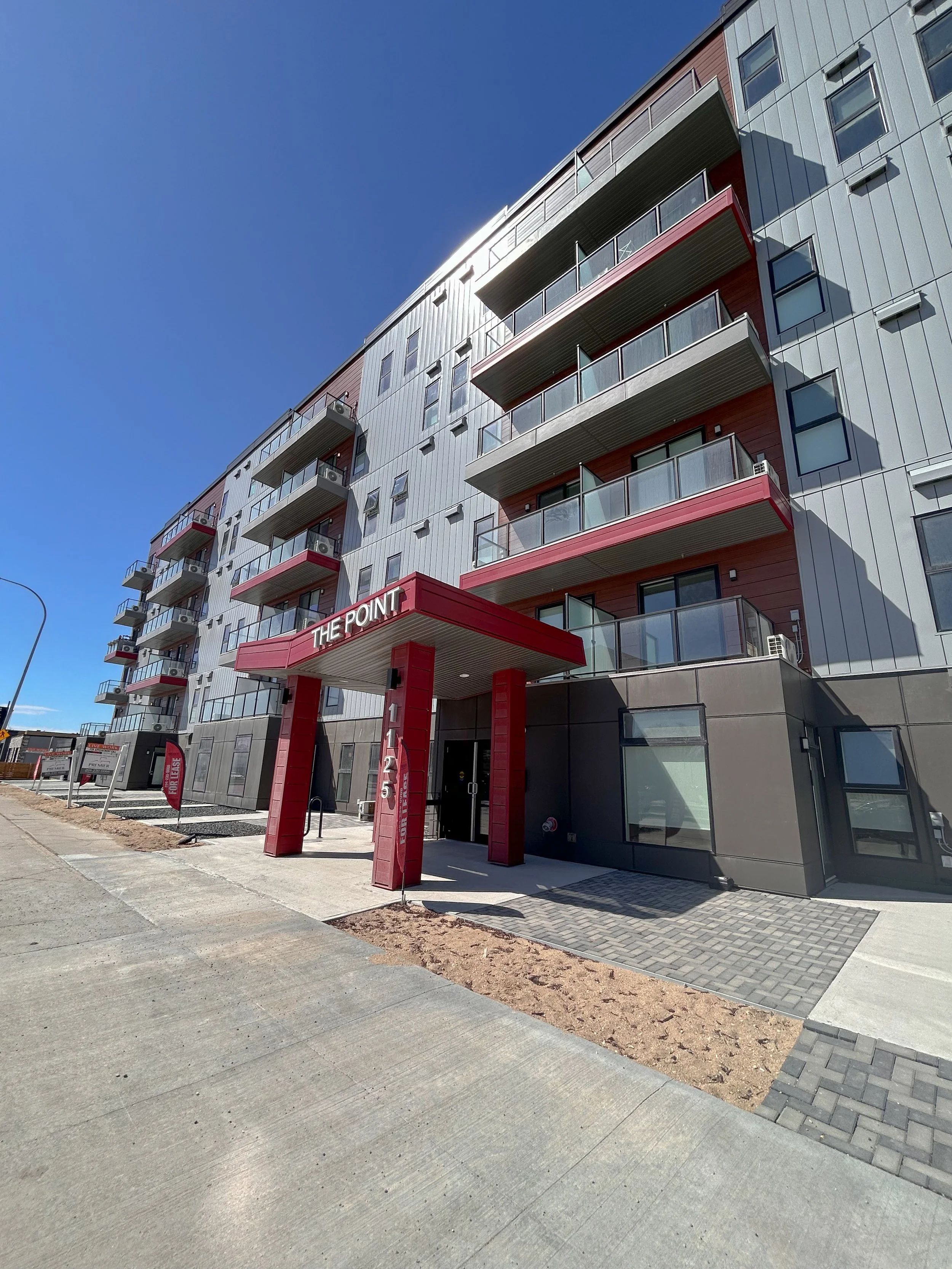 Exterior view of a modern multi-story apartment building with balconies, red accents, and an entrance labeled 'The Point' at 1125.