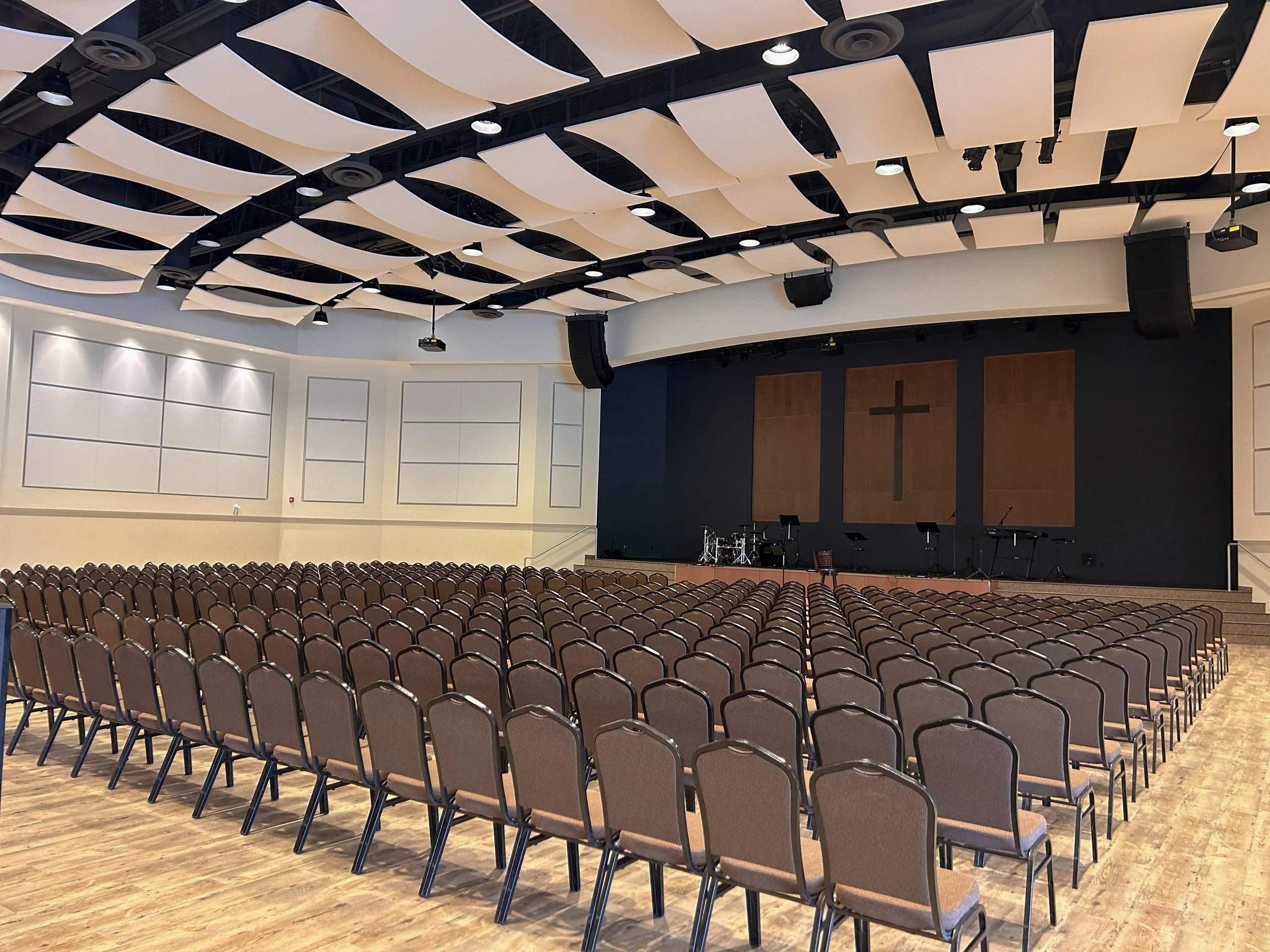 Empty auditorium with rows of chairs facing a stage with a cross, musical instruments, and microphones.