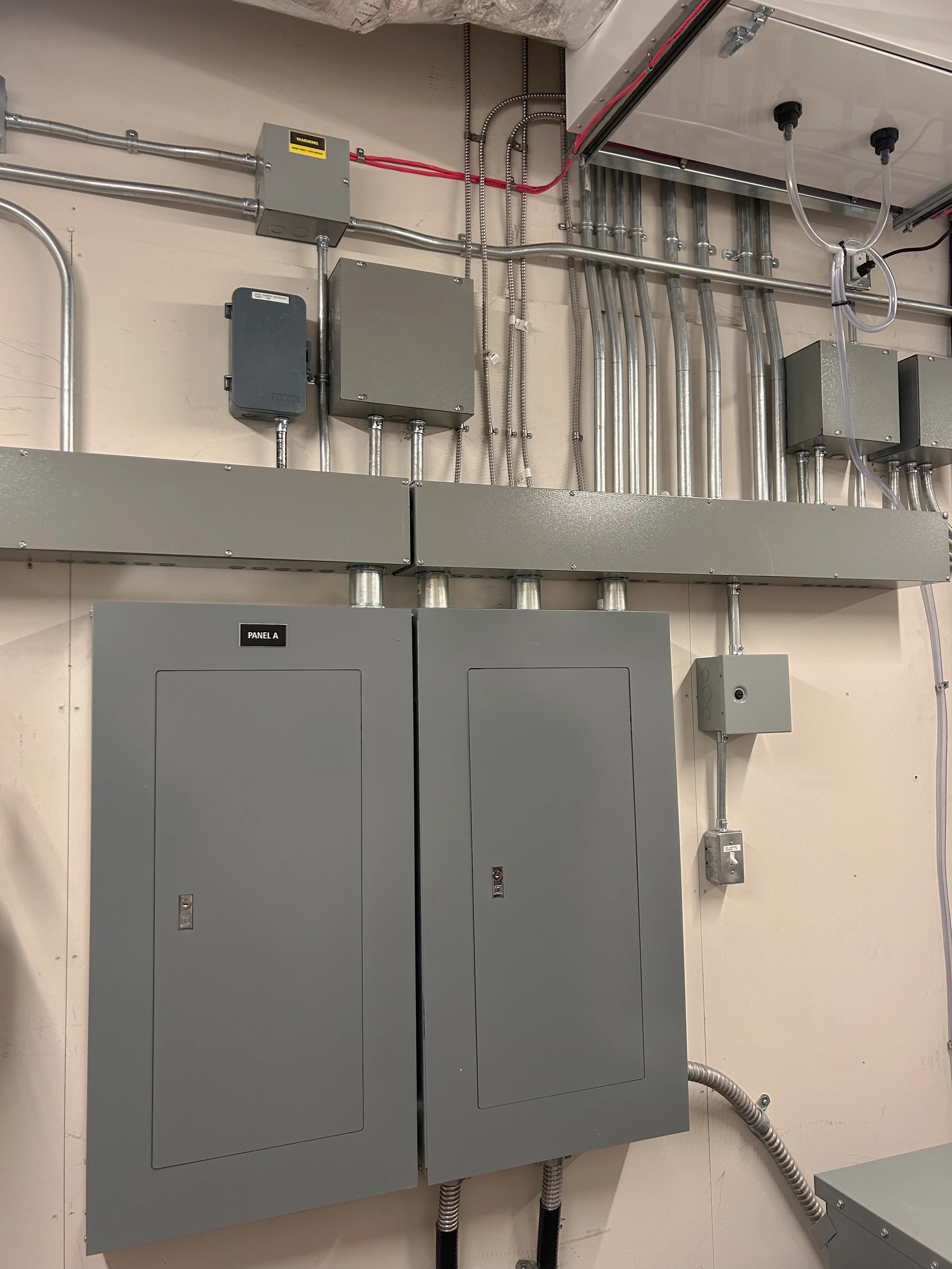Electrical panels and conduit pipes on a beige wall, with various junction boxes and wiring.