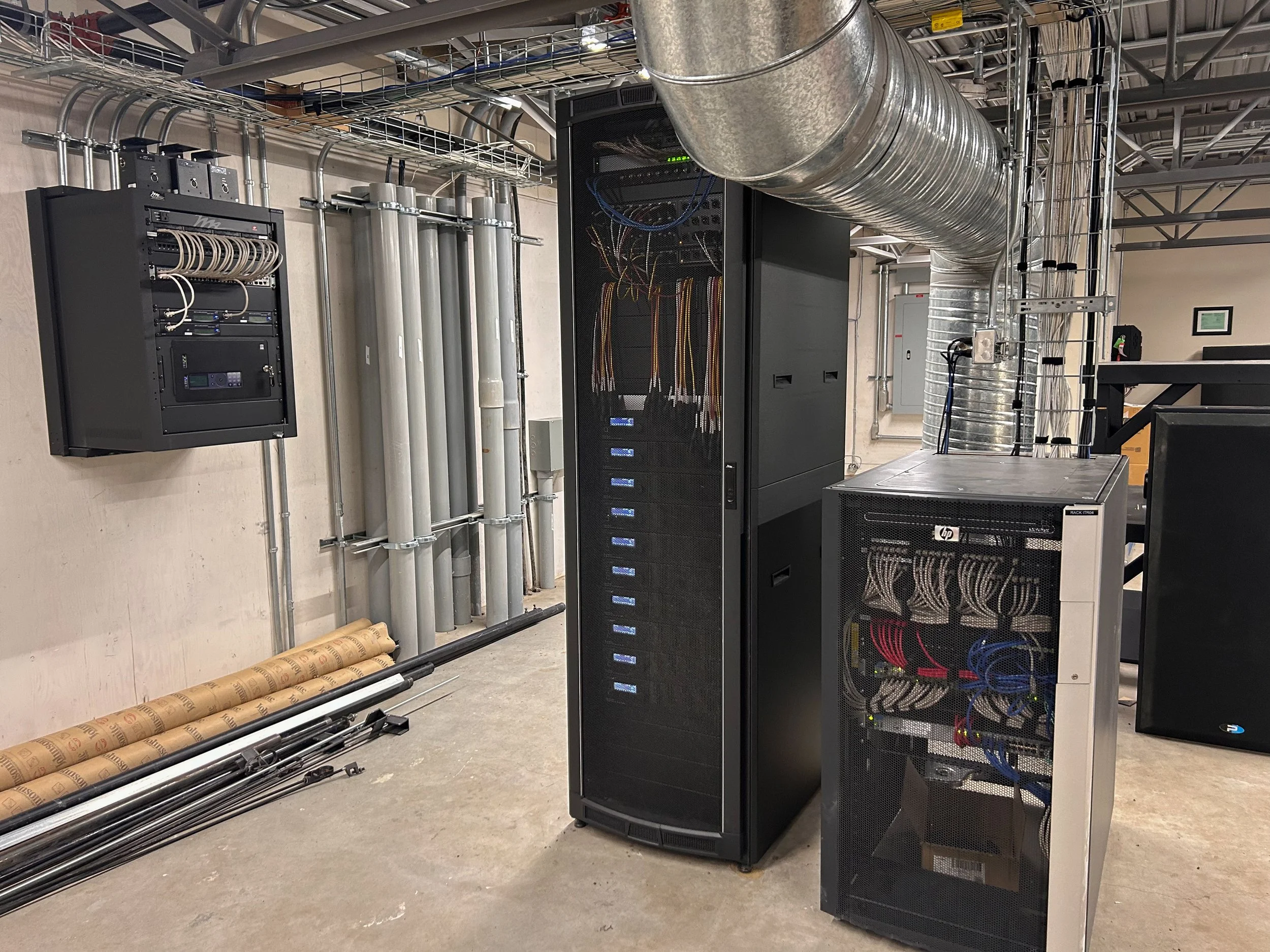 Data center with server racks, network cables, and HVAC ductwork overhead.