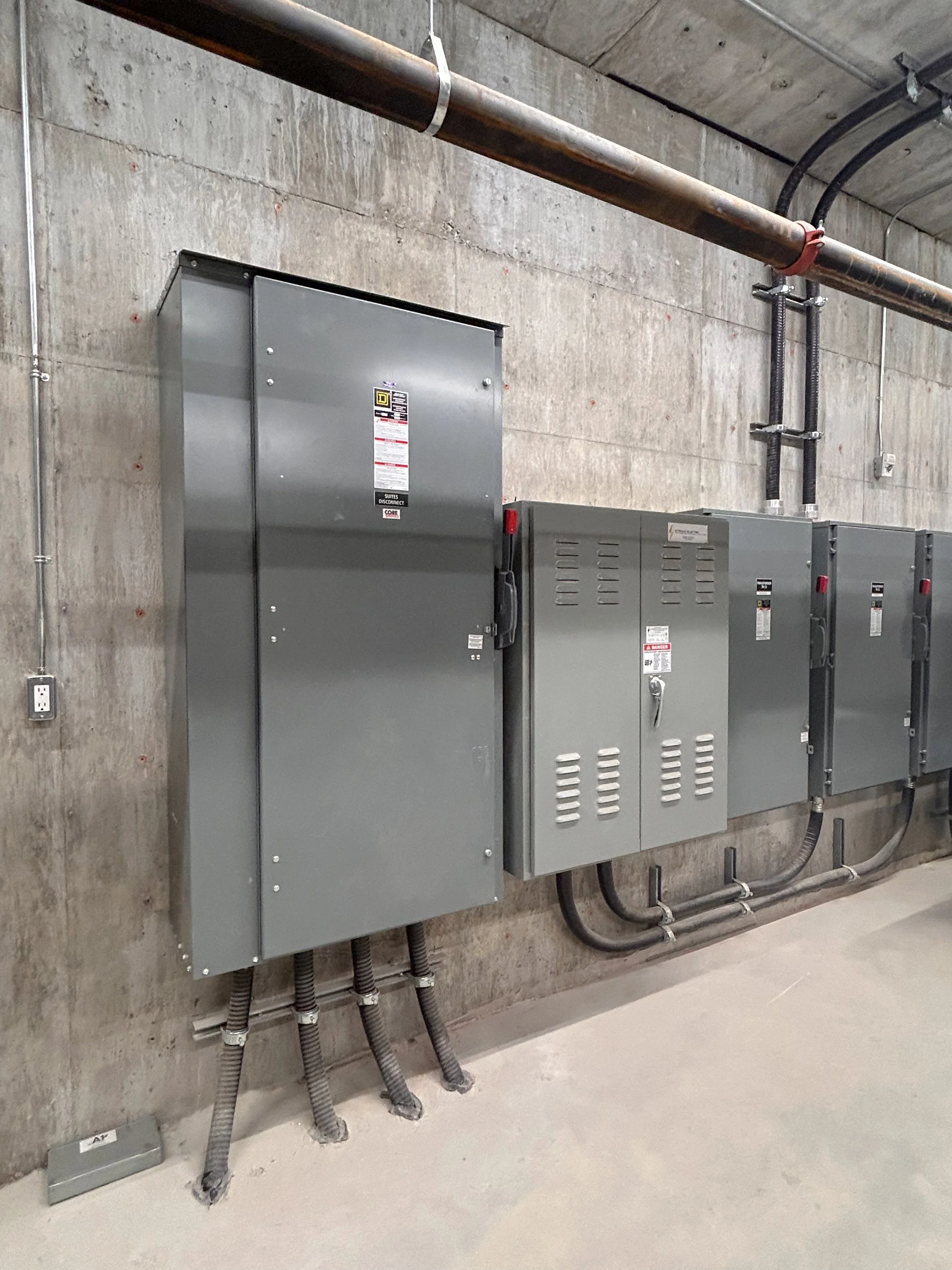 Electrical panels and meters mounted on a concrete wall in an industrial or utility room.