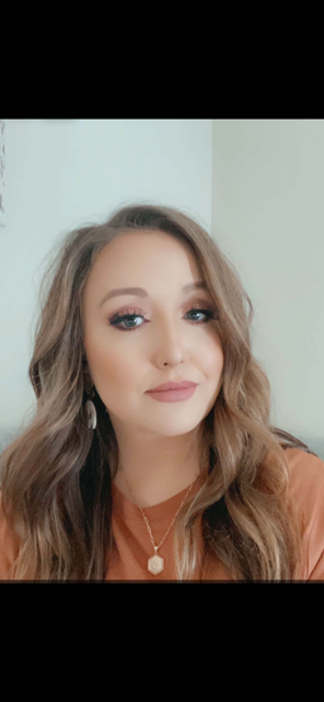 A woman wearing glasses and a turquoise top, resting her chin on her hand, with jewelry and bracelets, smiling softly.