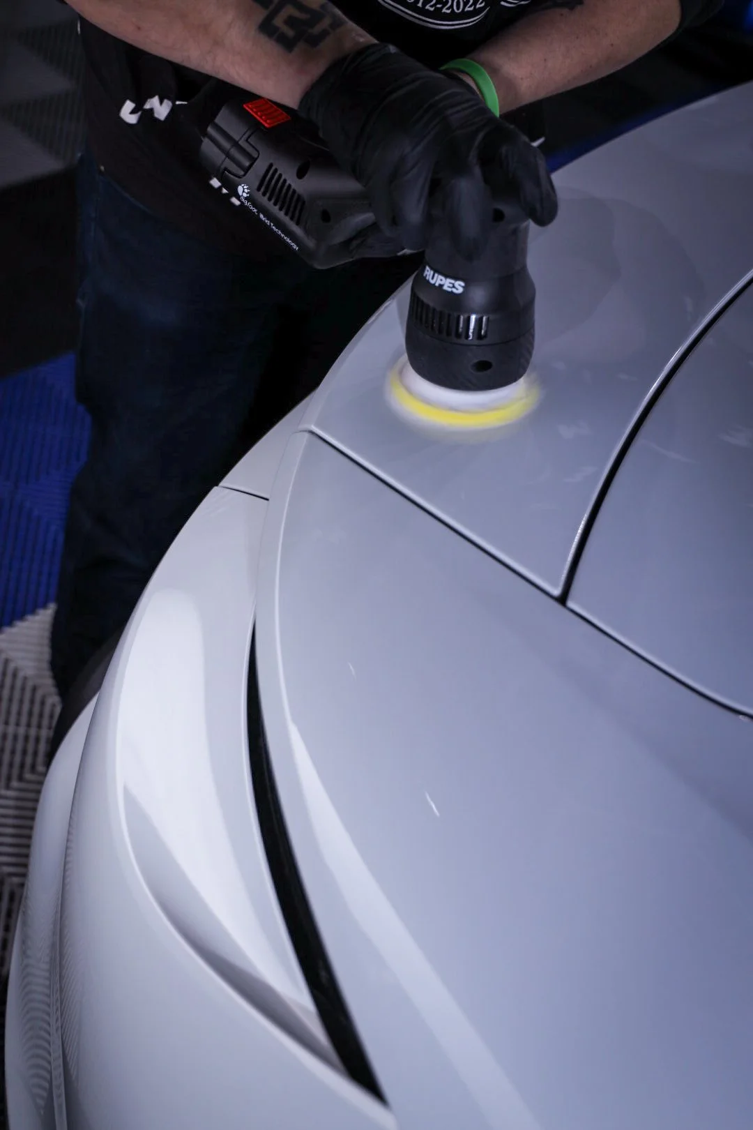 Person polishing a silver sports car with a power buffer