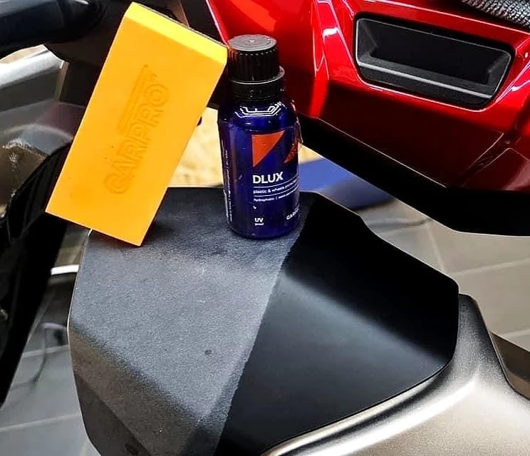 Botella de protector solar azul, esponja amarilla y parte de una motocicleta roja con un cascarón negro y gris