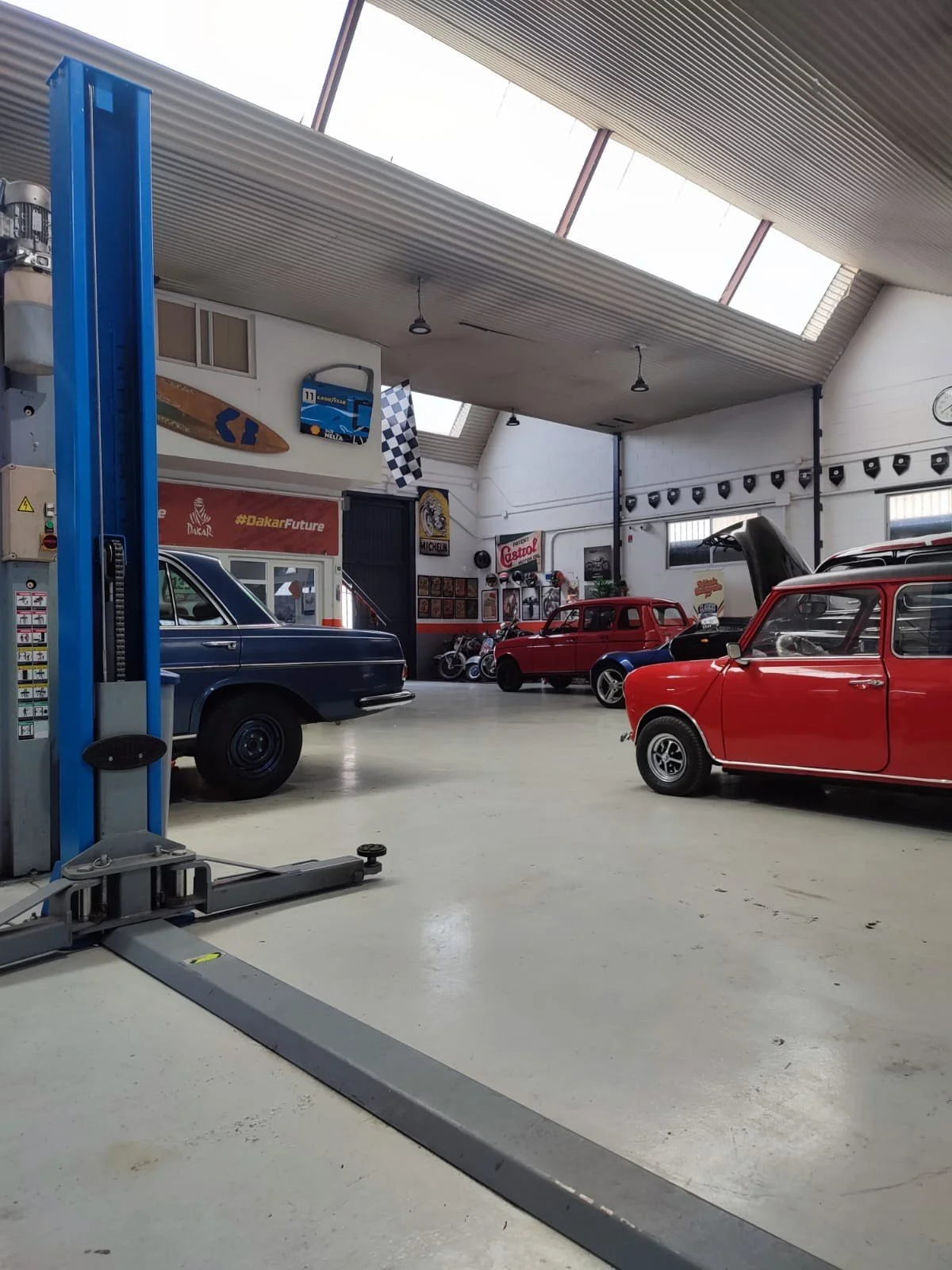 Interior of a vintage car garage with classic cars, posters, and racing memorabilia.