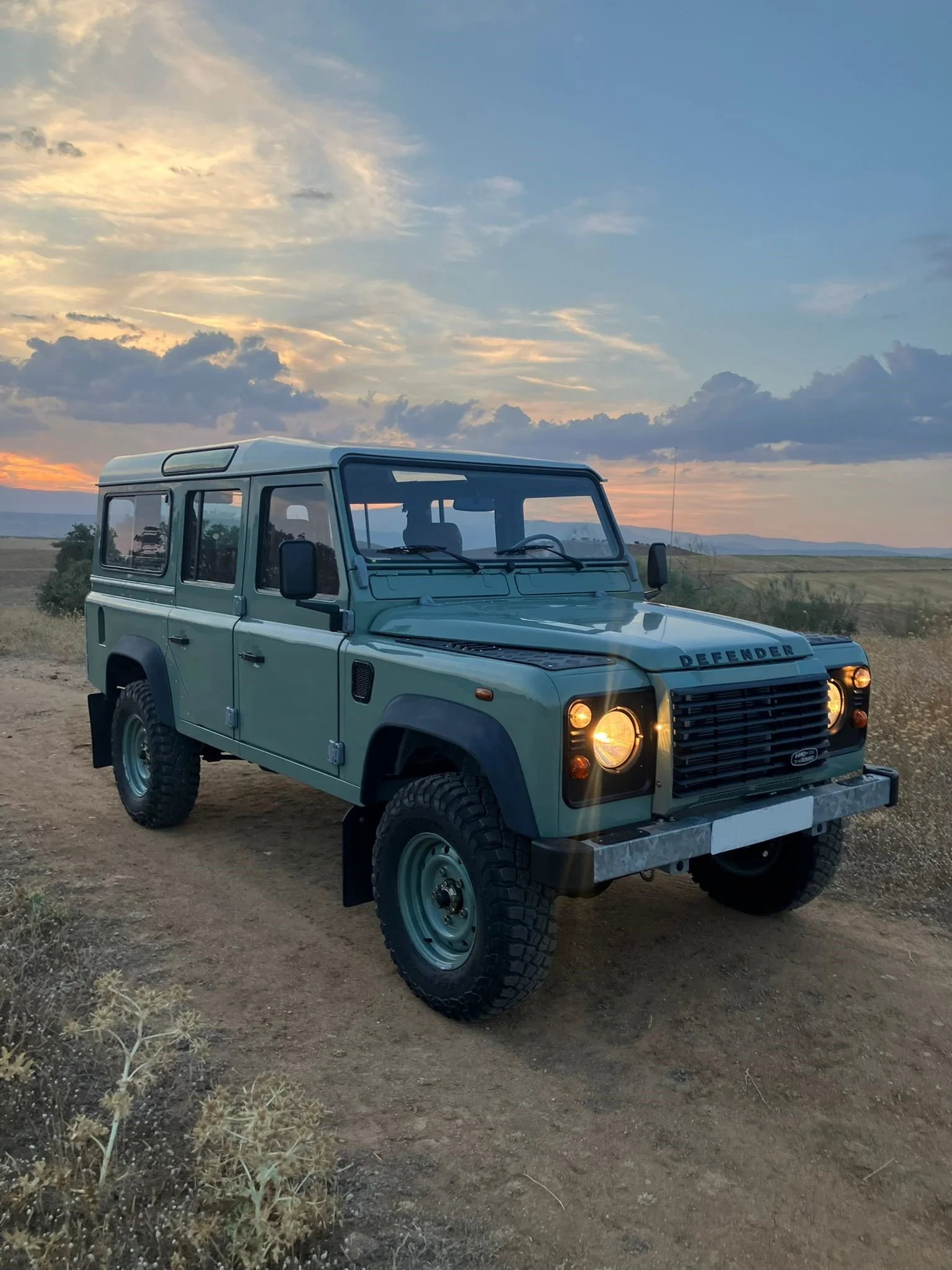 Vehículo todoterreno color verde en un paisaje natural al atardecer con cielo nublado