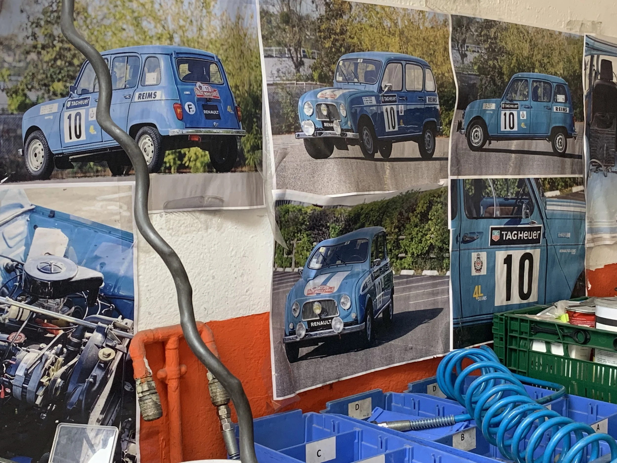Wall decorated with vintage racing car posters, including images of blue Renault and Citroën 2CV cars, along with some automotive parts and tools in the foreground.