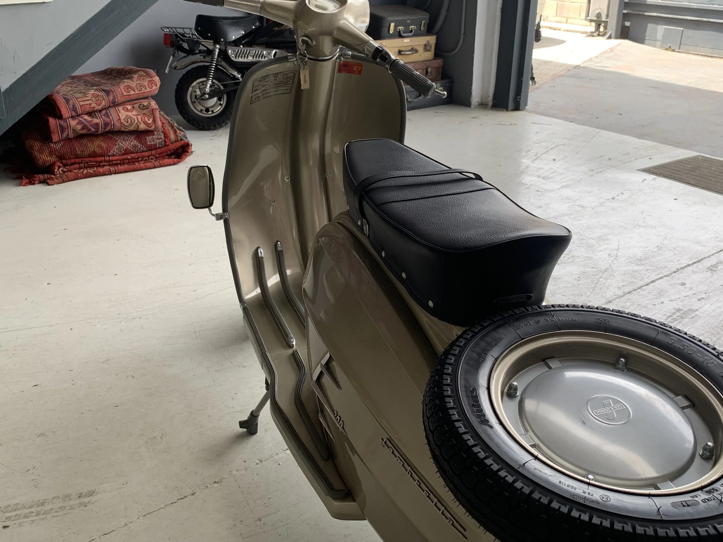A vintage beige scooter with a black seat and a spare tire mounted on the back, parked inside a garage.