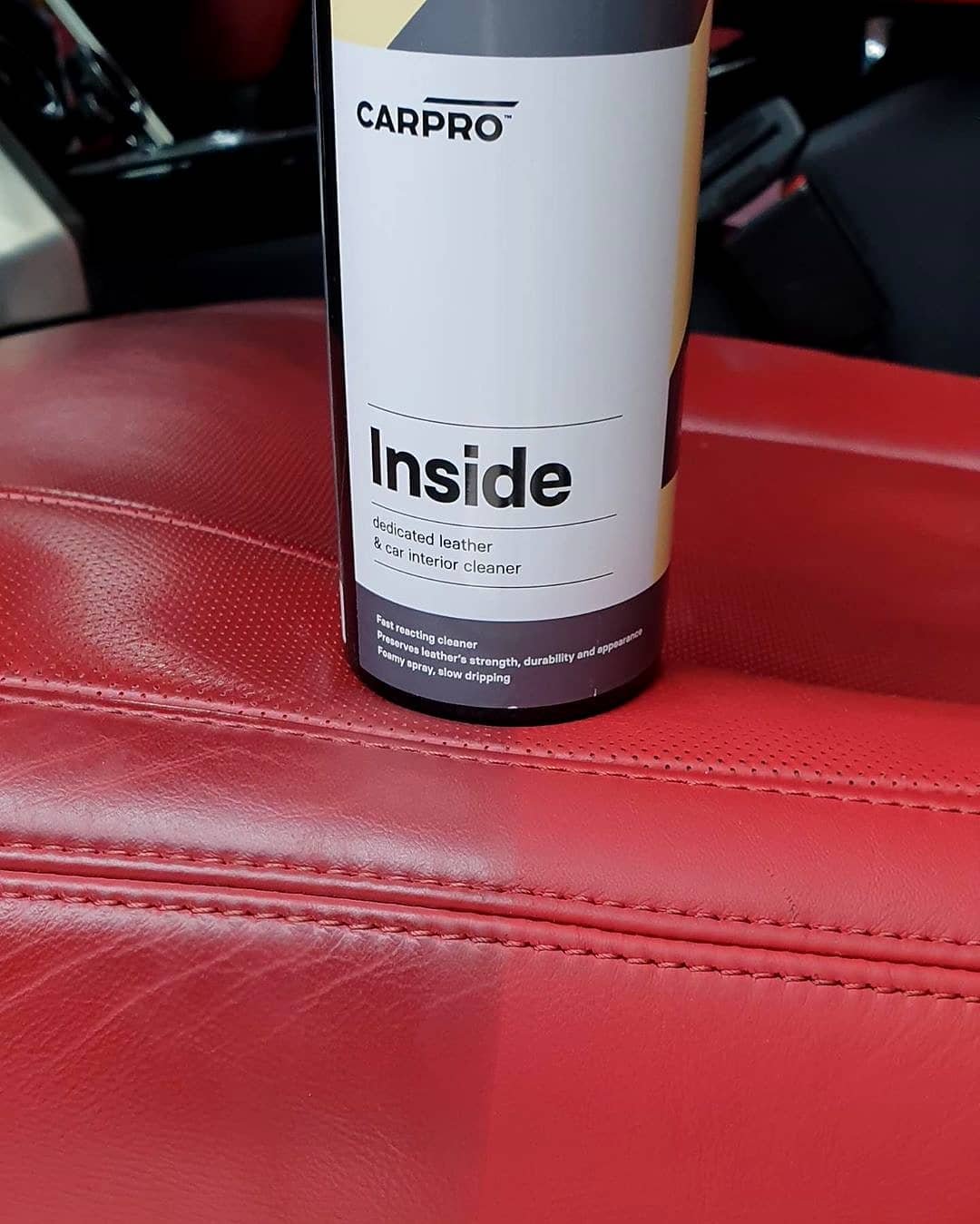 A container labeled 'Inside' dedicated leather and car interior cleaner, placed on a red leather surface in a vehicle.