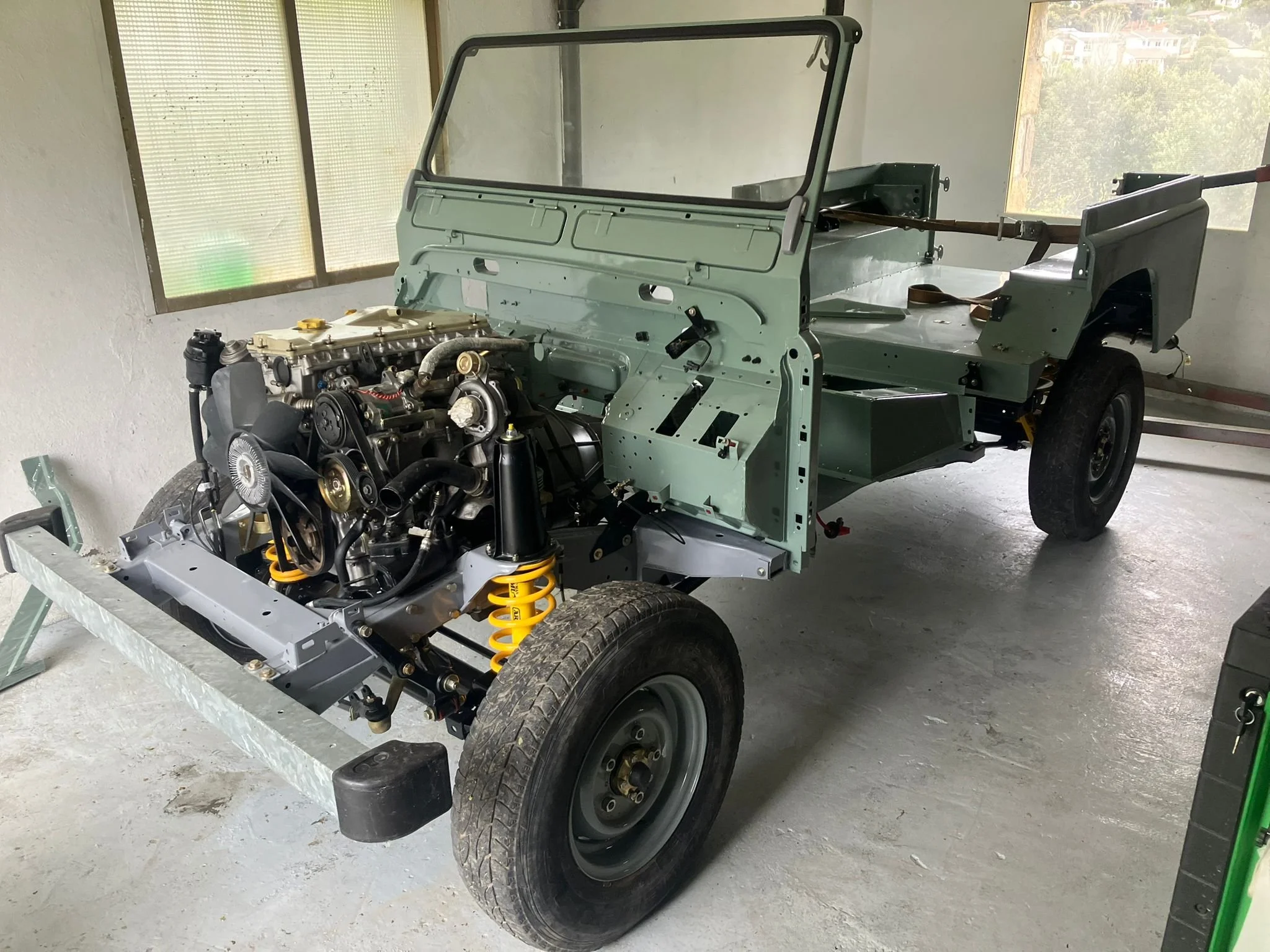 Chasis de automóvil en proceso de ensamblaje, con motor instalado en la parte delantera y llantas montadas, en un taller de construcción de vehículos.