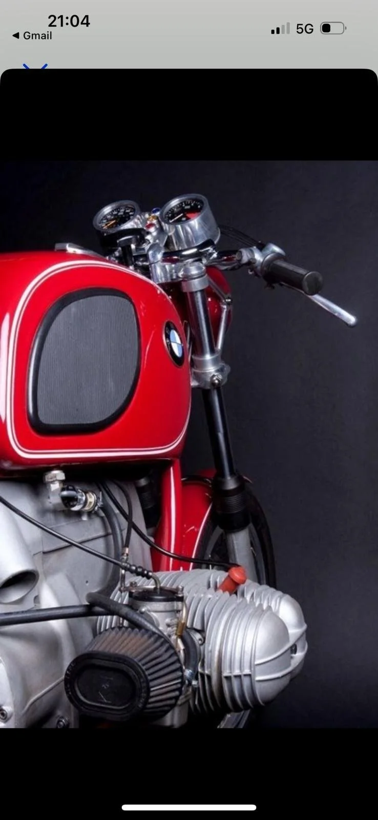 Vista frontal de una motocicleta clásica BMW con tanque rojo y motor en primer plano, fondo negro.