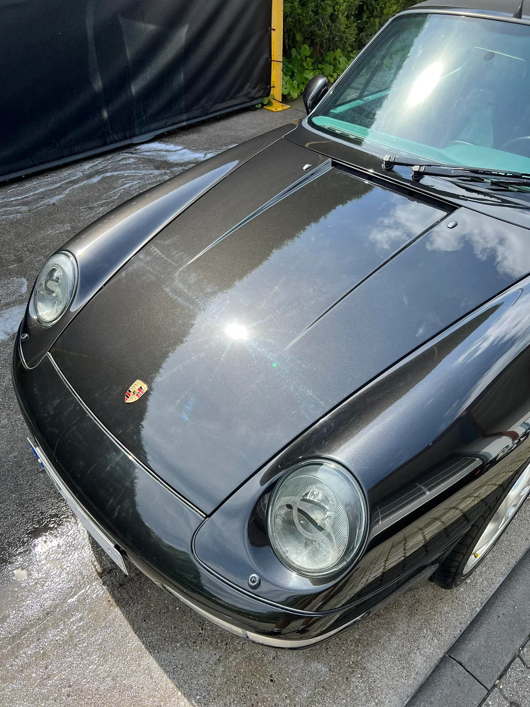 Auto Porsche clásico de color negro, visto desde la parte delantera, con el capó visible y reflejo del cielo y algunas nubes en el parabrisas.