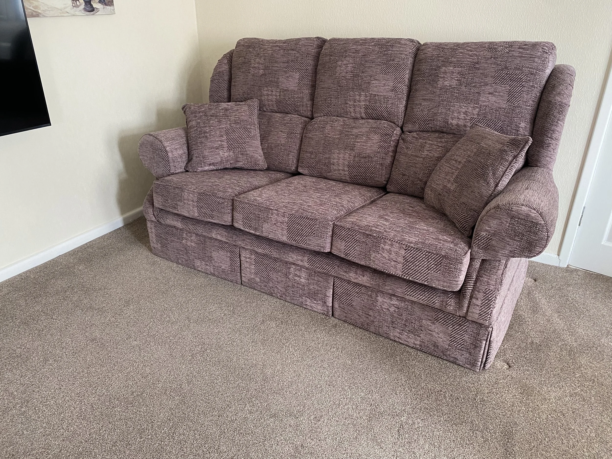 A pinkish patterned fabric sofa with matching throw pillows in a room with beige carpet and cream walls.
