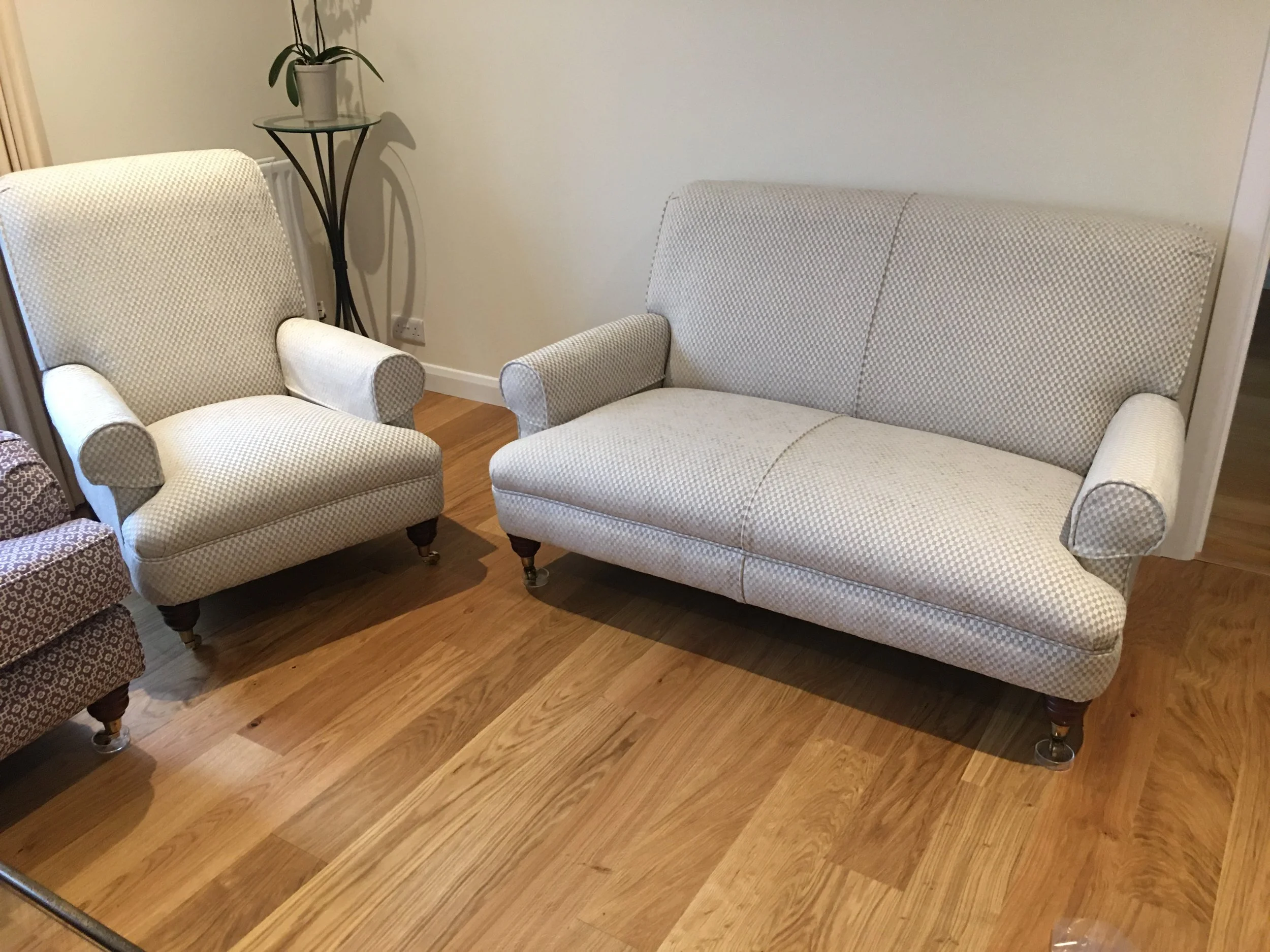 A living room with a beige armchair and a matching beige loveseat, both with rolled arms and dark wood legs on a wooden floor.