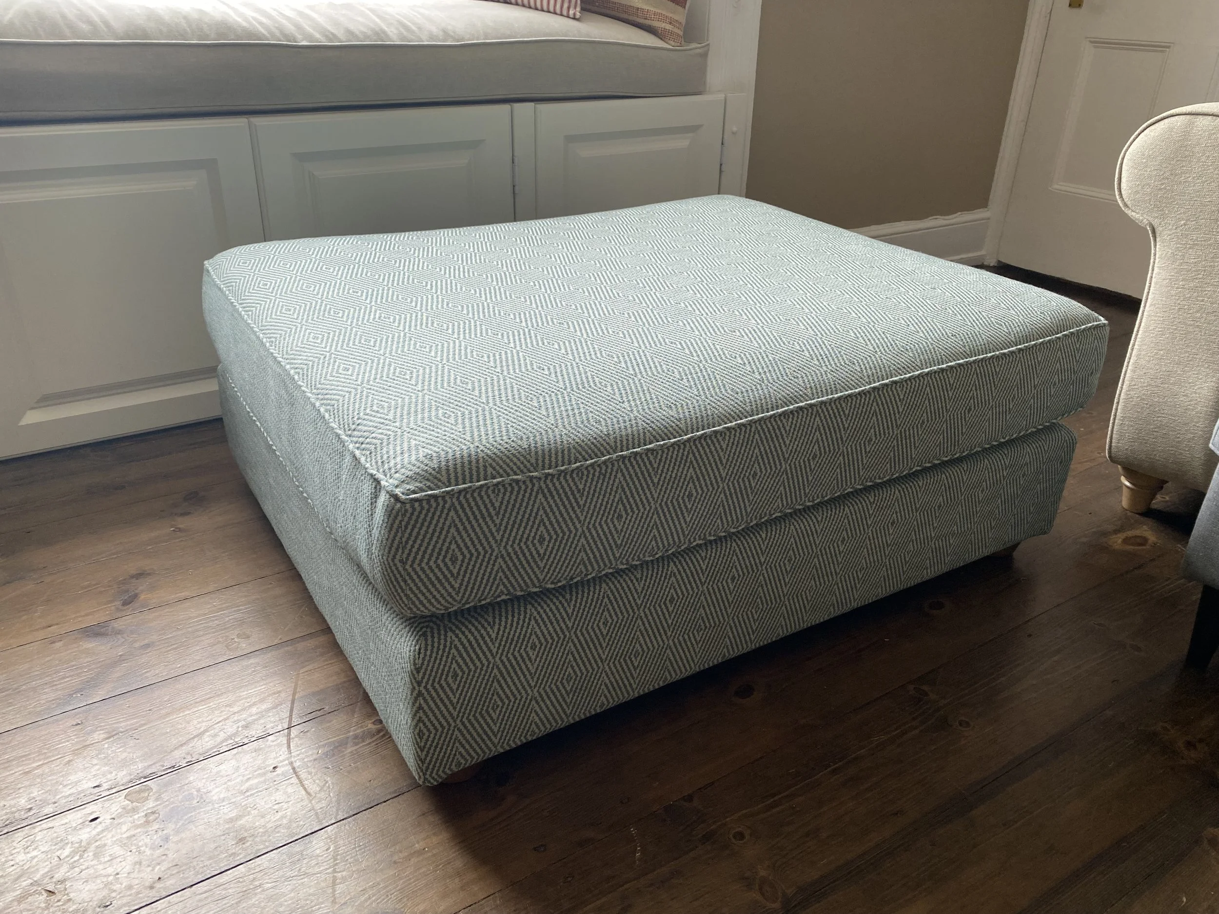 A large upholstered ottoman with a patterned fabric in a living room with hardwood floors.
