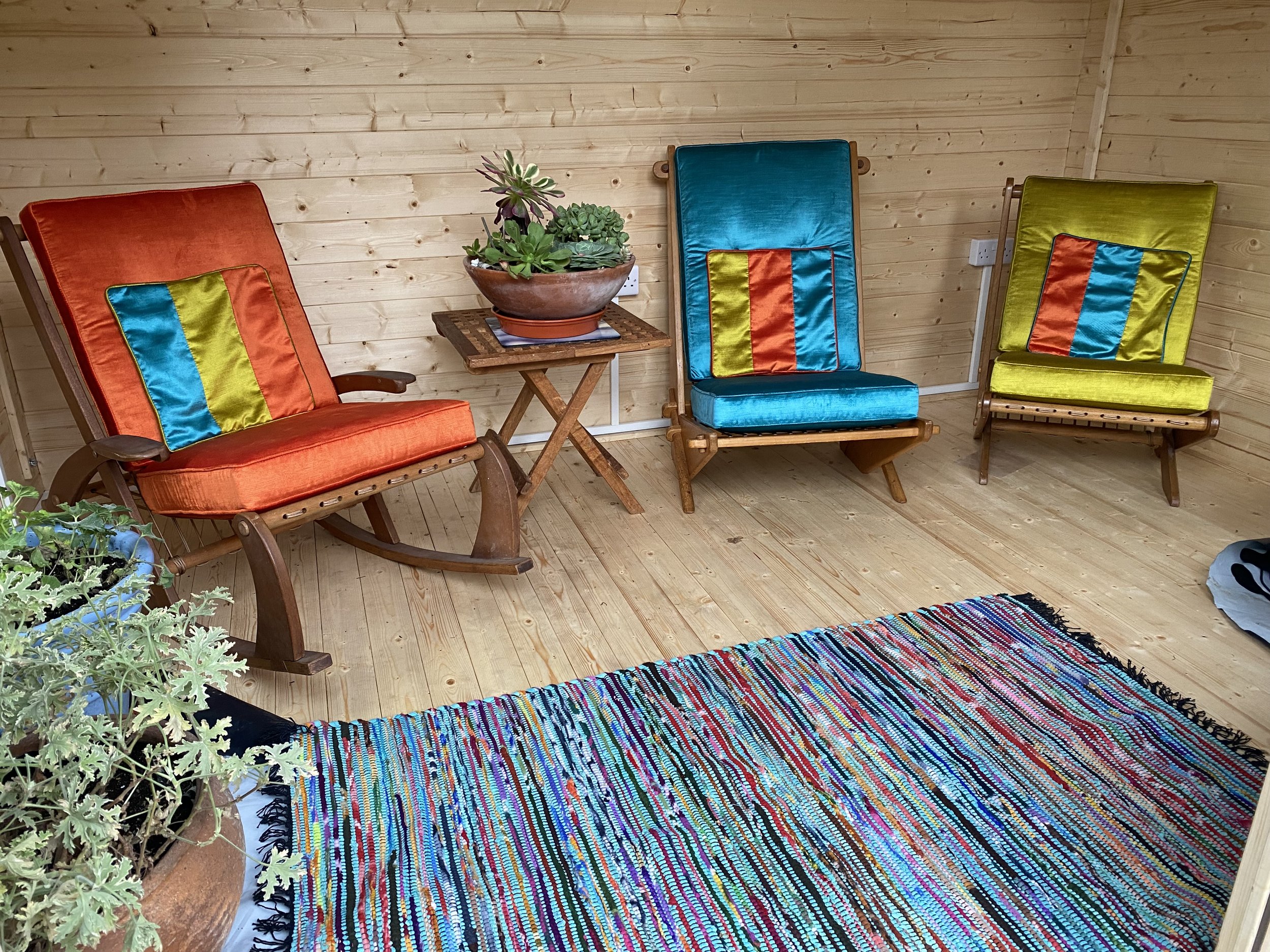 Cozy wooden room with colorful chairs, a small table with a plant, a woven rug, and a potted plant.