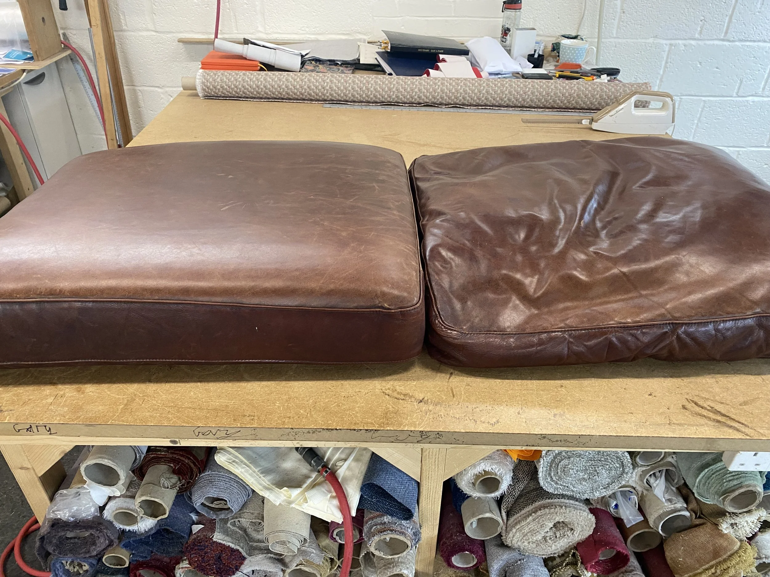 Two vintage leather cushions on a workbench showing a newly refilled one on the left and an original saggy one on the right..